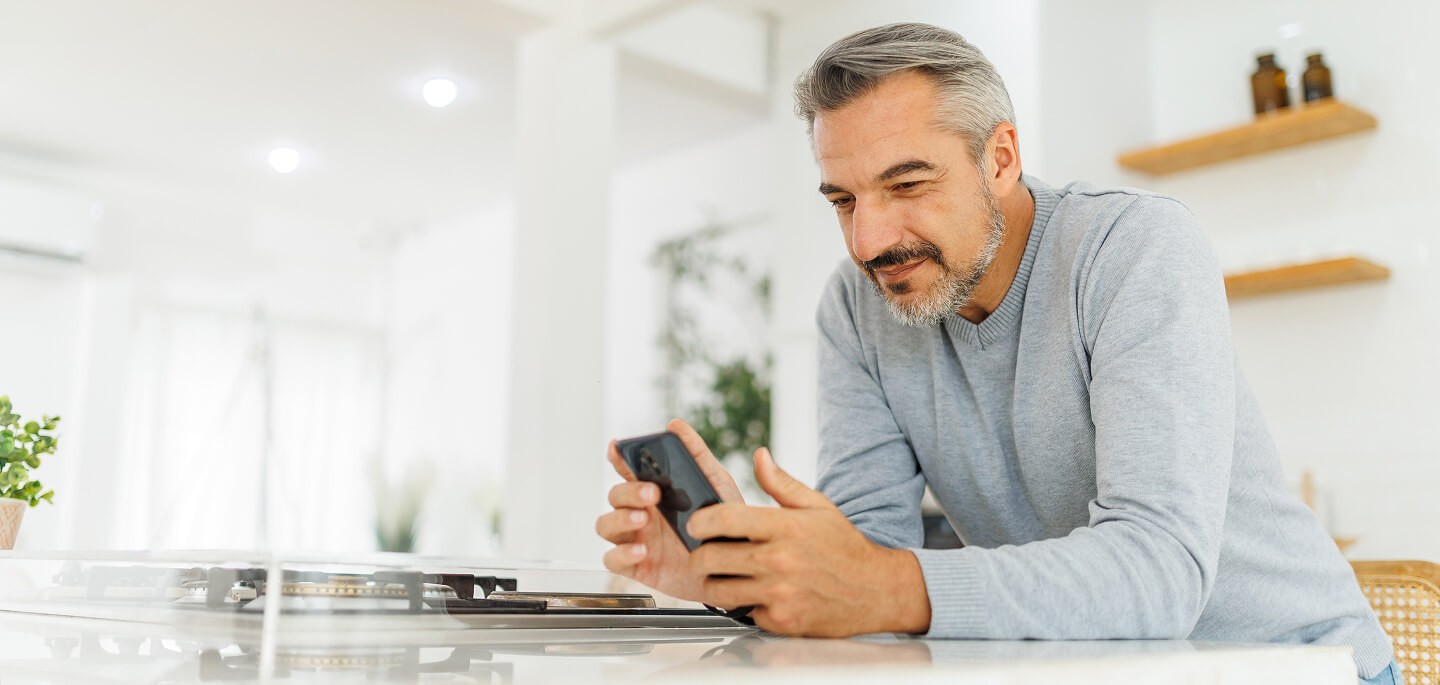 Older man looking at his phone in the kitchen.