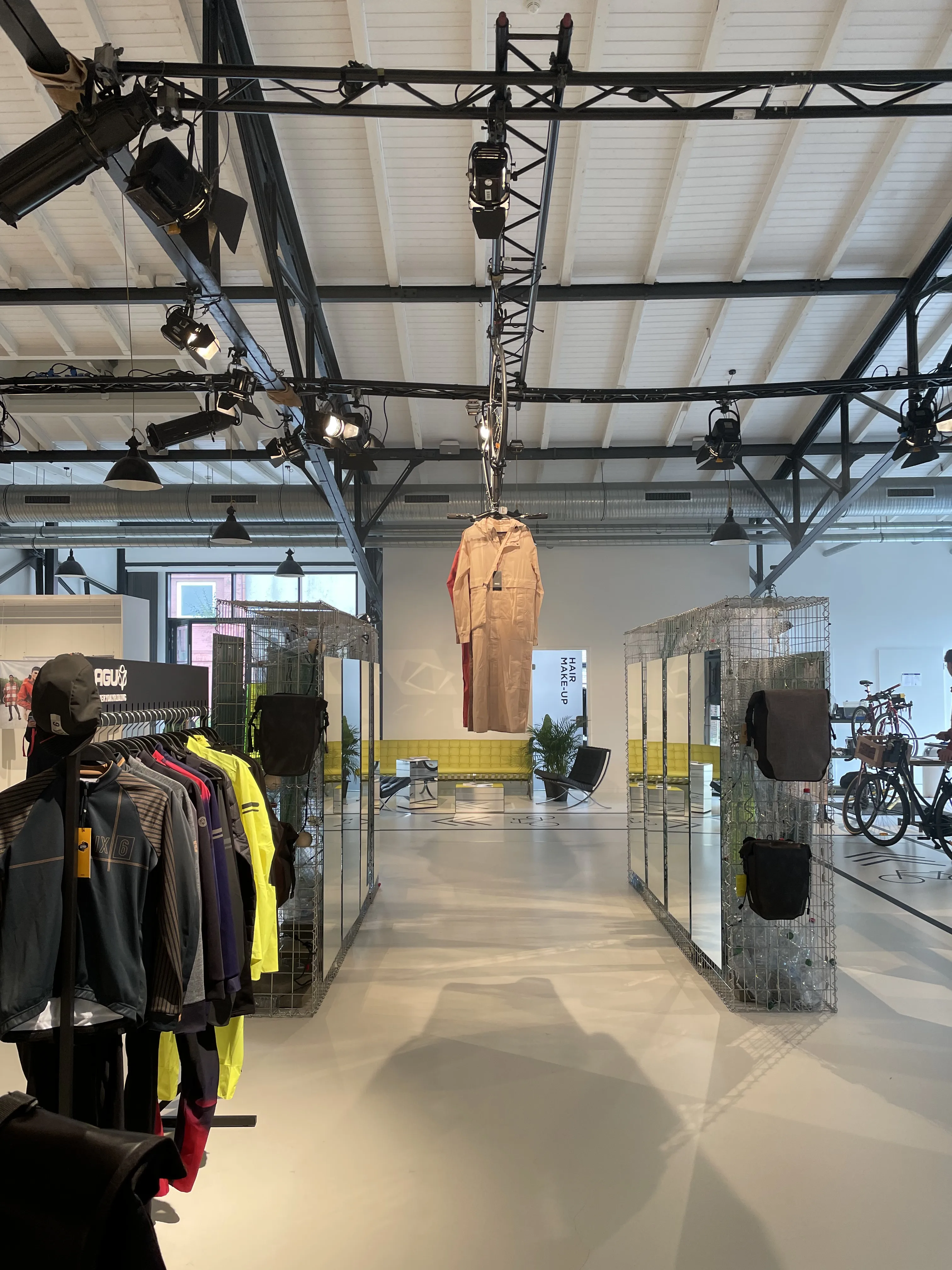 Bright AGU showroom with black truss ceiling, wire-mesh displays, mirrors and cycling apparel on racks.
