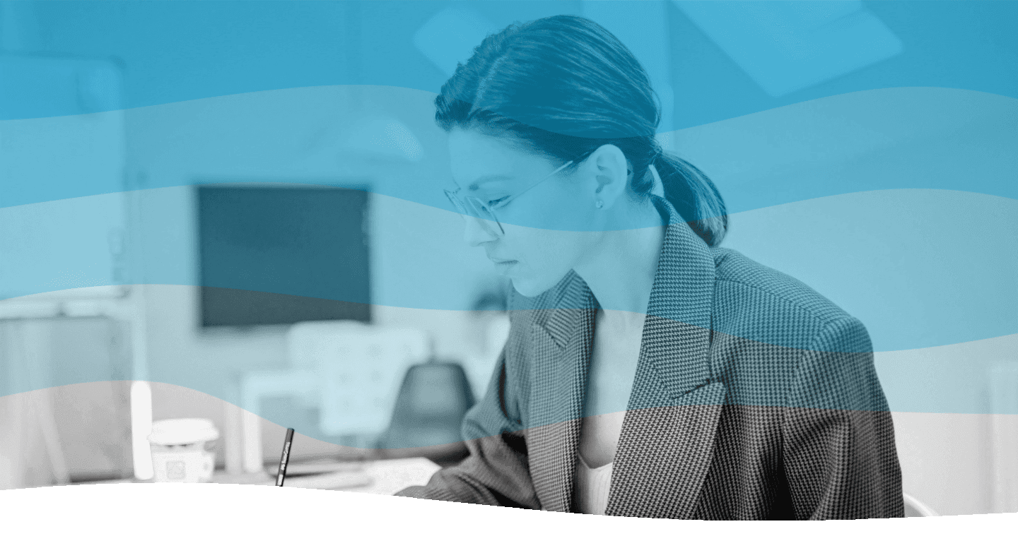 A person wearing glasses and a checkered blazer is working intently at a desk in a modern office setting, with blurred office furniture visible in the background, overlaid with a translucent blue wave pattern.