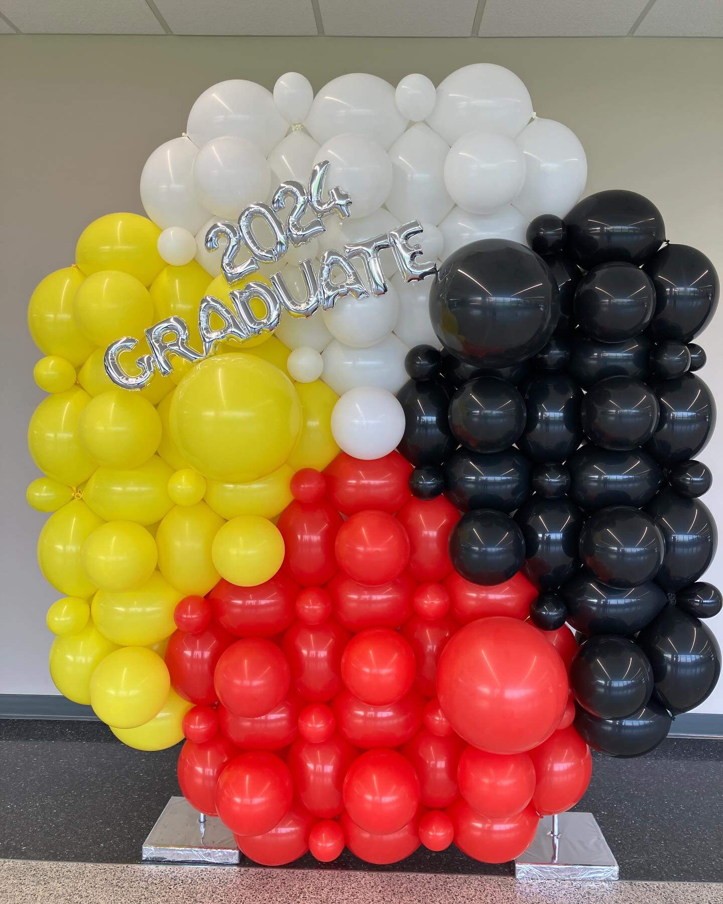 alloon wall with yellow, white, red, and black balloons spelling out the word GRAD for a graduation event by Be Bold Balloons