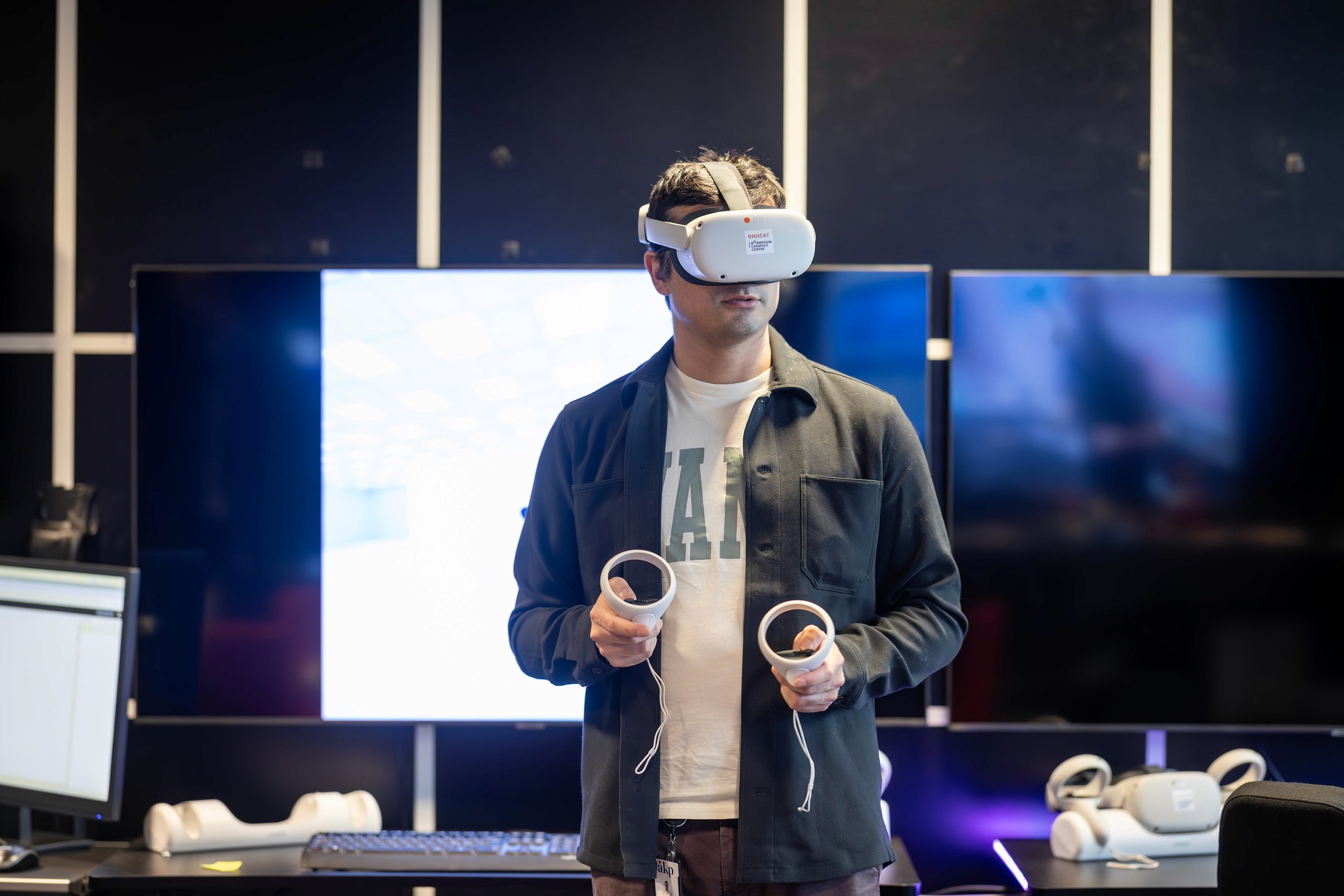 A person wearing a virtual reality headset stands in front of multiple screens, engaged in a digital experience.
