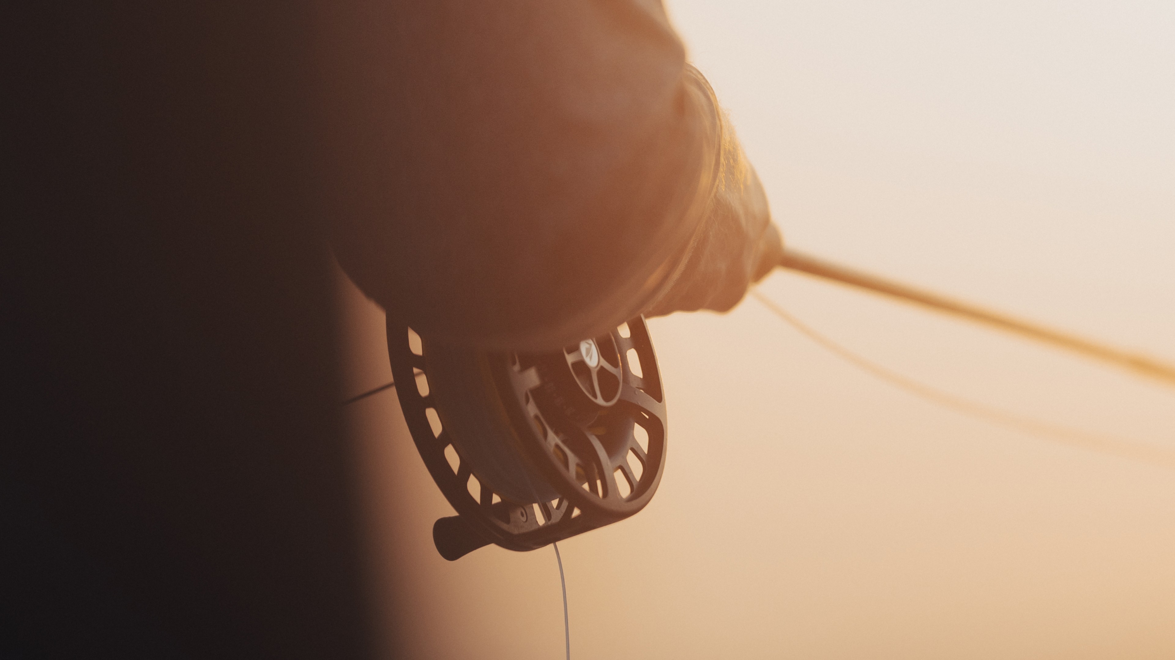 Closeup of a person holding a fly fishing rod and reel in glowing warm sunlight