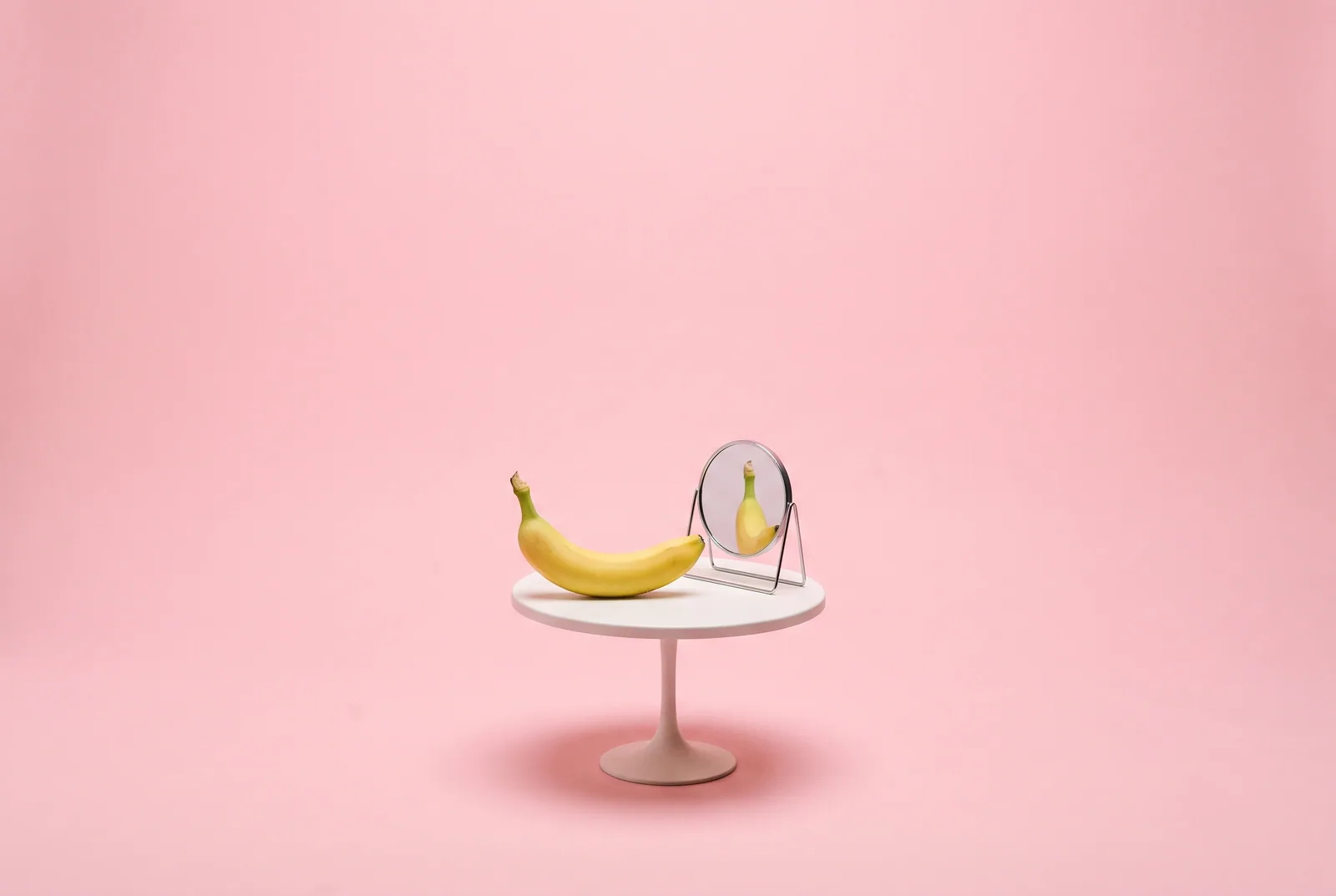 A banana alone at a tiny café table facing a small mirror, the loneliness loop of AI companions