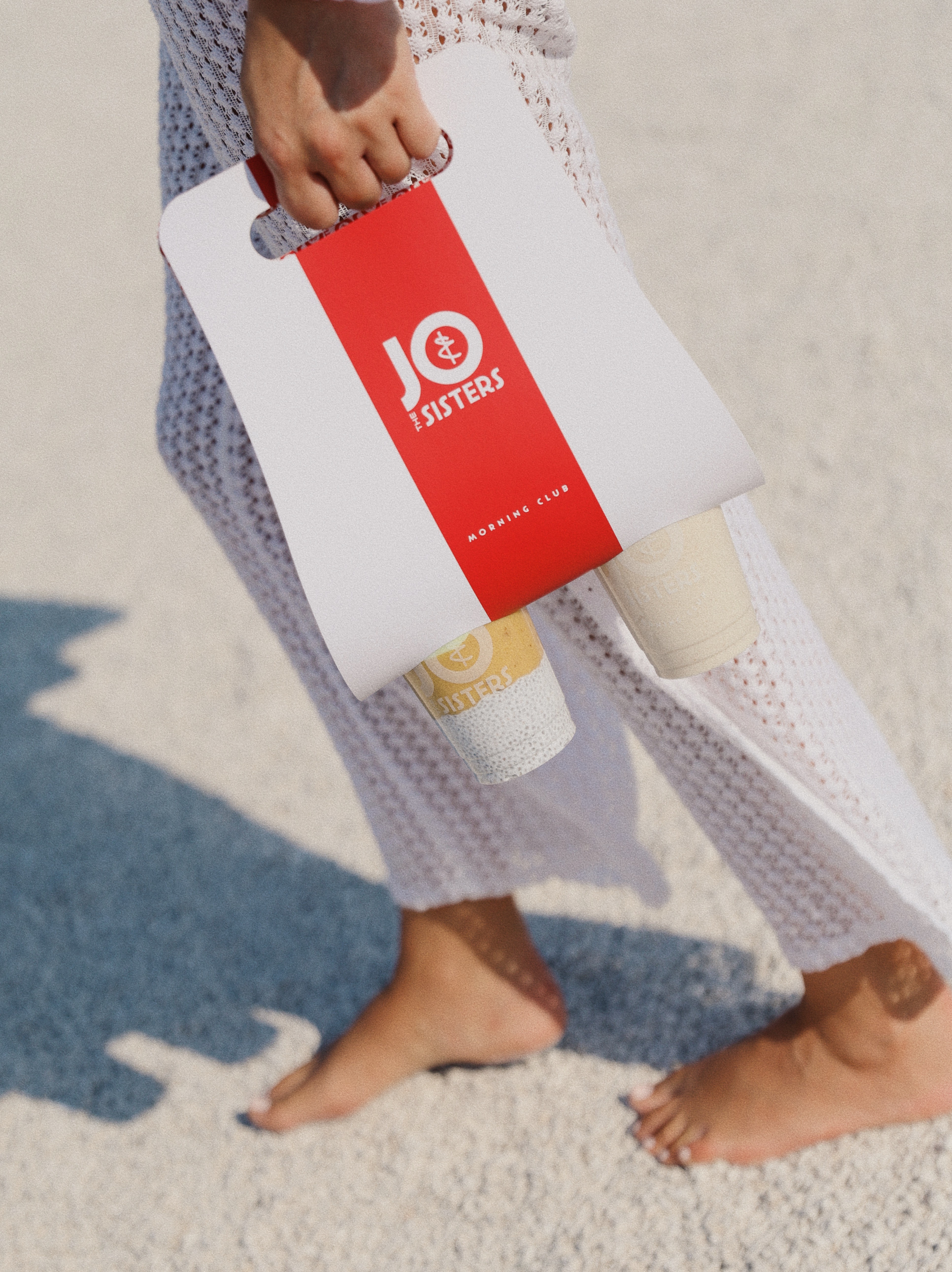Jo & The Sisters Morning Club grab-and-go drinks carried in branded takeaway packaging on a sunny d