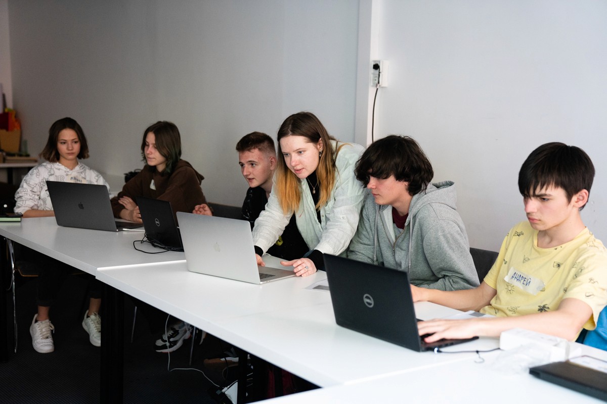 Gruppe junger Menschen, die an Tischen sitzen, an Laptops arbeiten und auf ihre Bildschirme schauen.