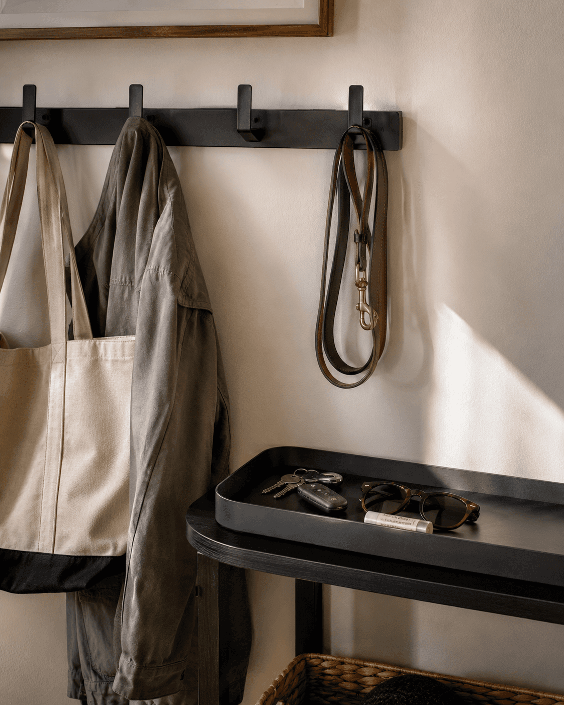 Close up shot of an entry tray with keys & sunglasses, a wall hook with a leash, coat & bag.