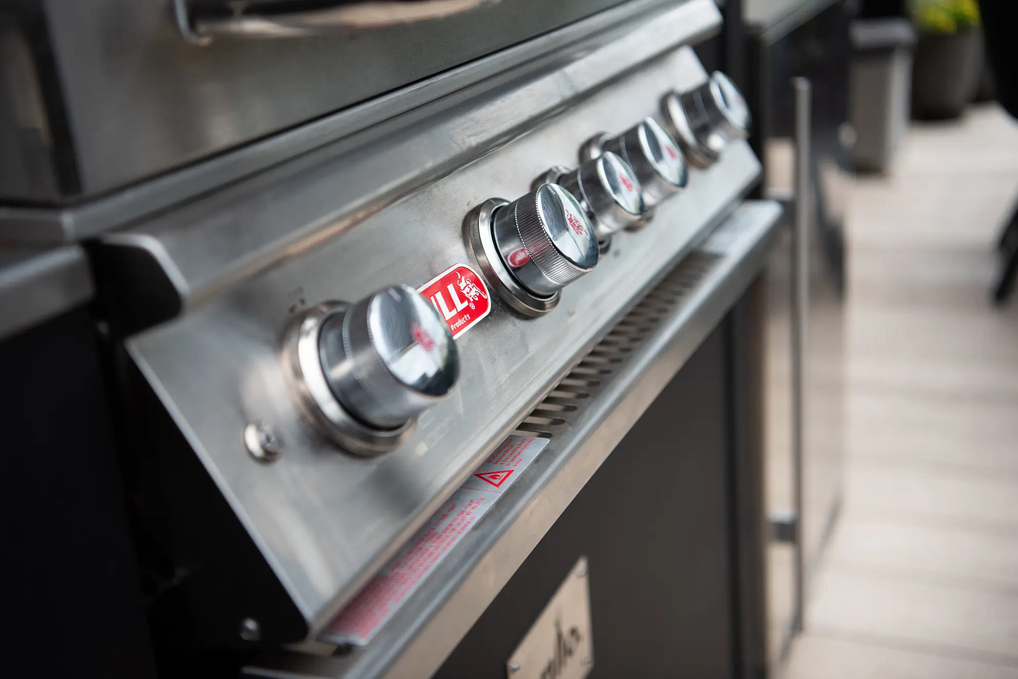 Close-up of a modern gas grill showing four control knobs and sleek metallic finish.