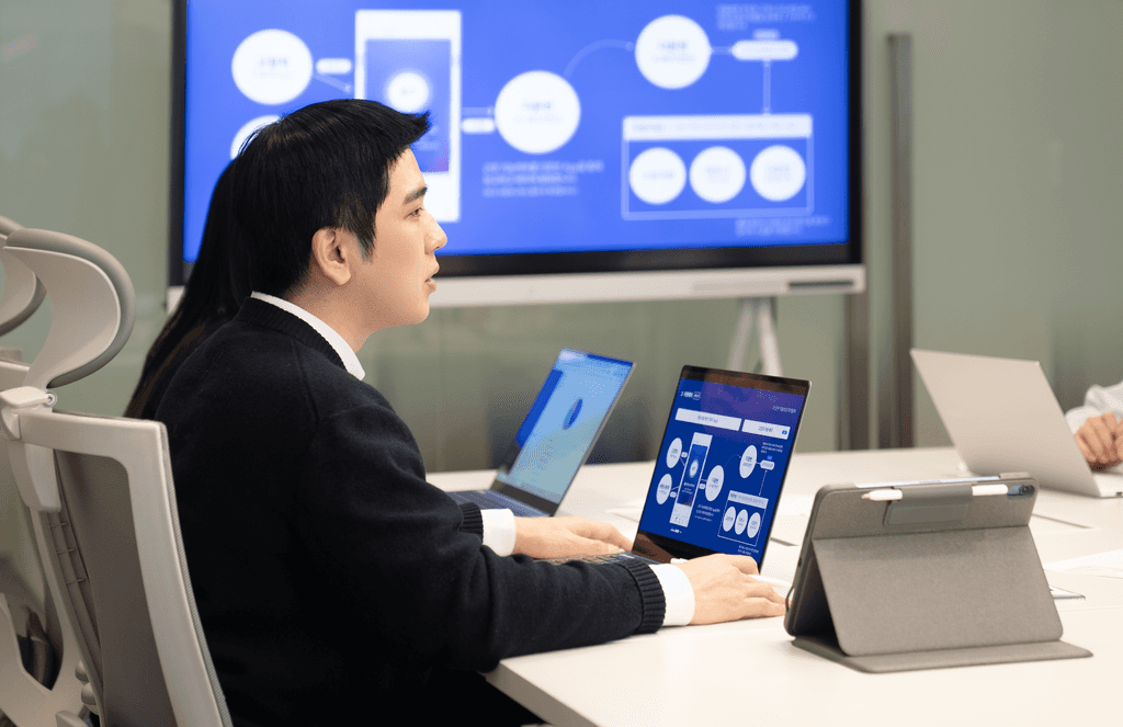 CJ대한통운 더 운반 전문가가 태블릿과 노트북으로 운송 시스템 구조도를 검토하며 서비스를 설명하고 있는 모습입니다. 파편화된 운송 시스템과 현장 이슈를 진단하고 운임 최적화 개발까지 지원한다는 문구가 하단에 표시되어 있습니다.