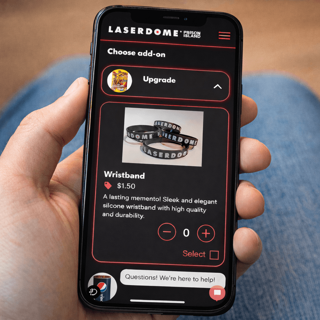 A young person with curly hair smiles at the camera while sitting in front of a laptop against a dark background.