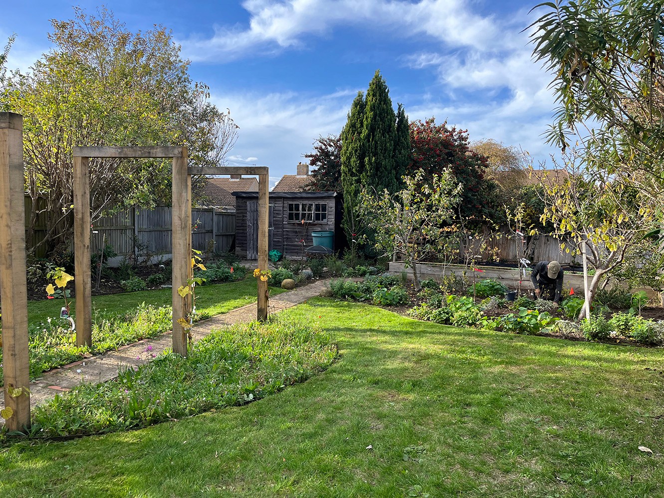 A sunny garden scene with grass, trees, and a light blue sky dotted with clouds.