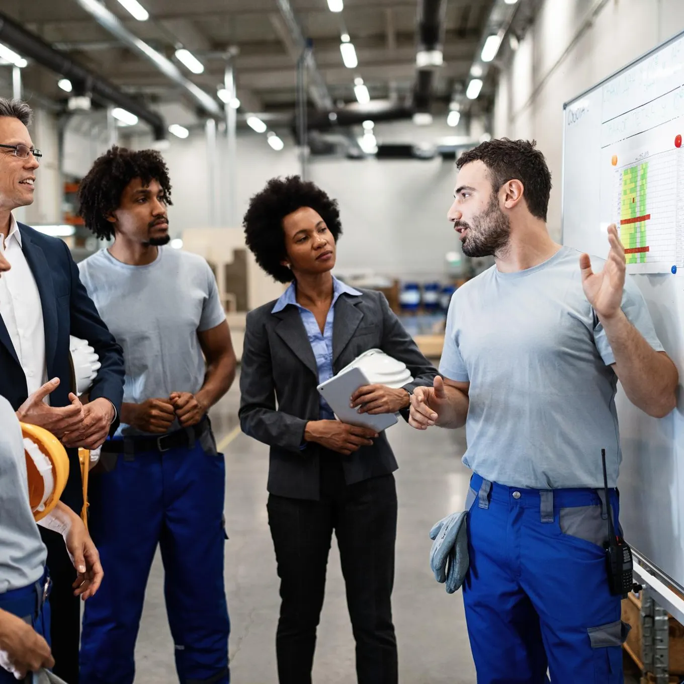 Chef d’équipe anime un brief devant un tableau, collègues et responsable écoutent dans un atelier.