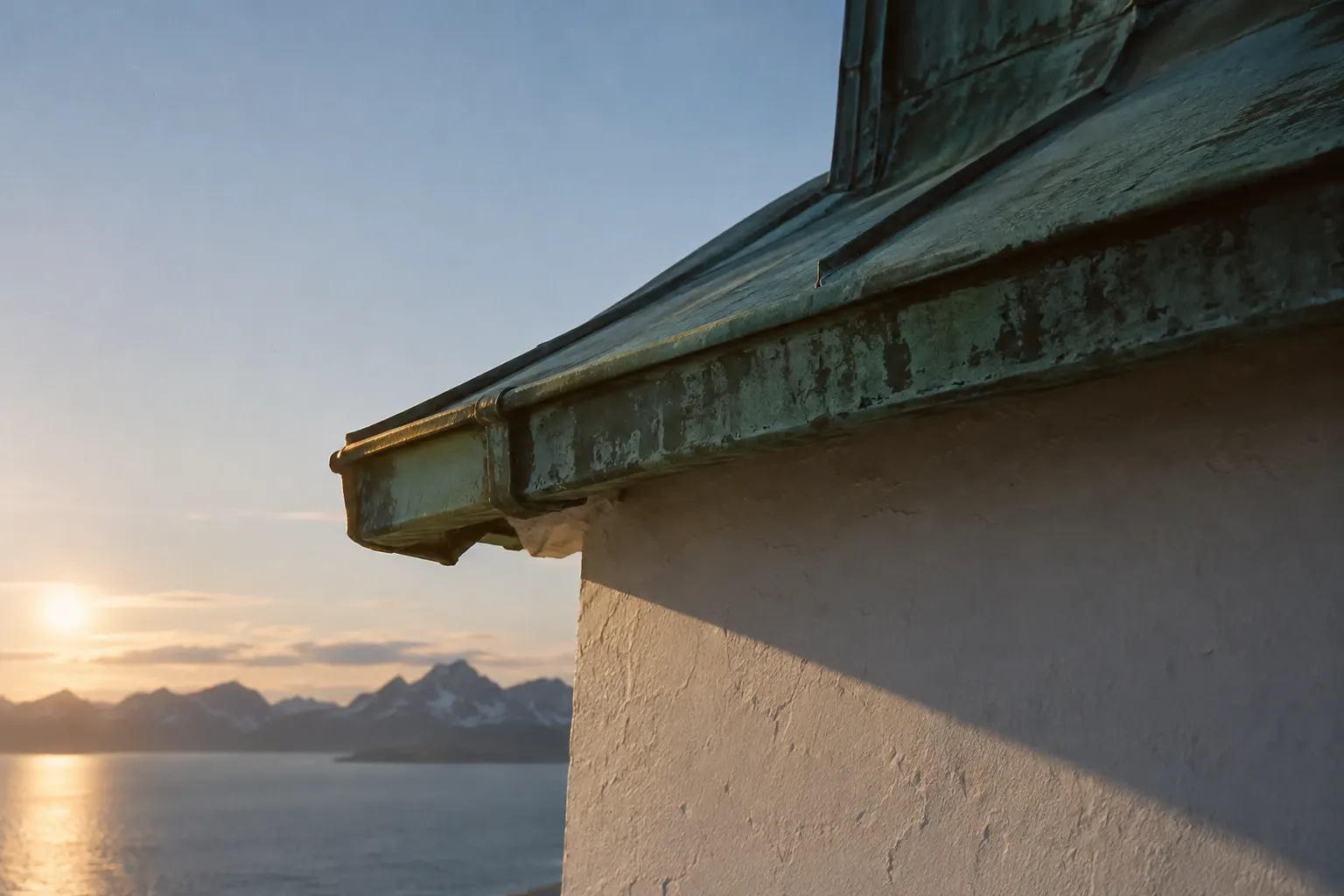 A green copper roof edge against a white wall with a diagonal shadow.