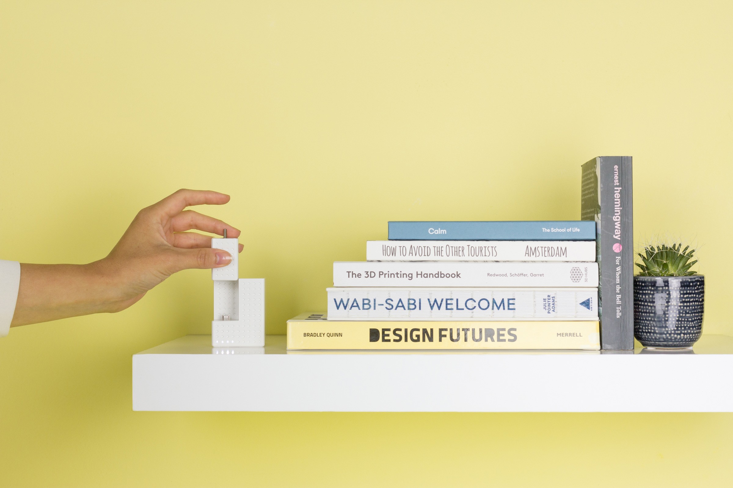 Image of a hand placing a Smartian in its charging base which is positioned on a book shelve with various books and a small plant