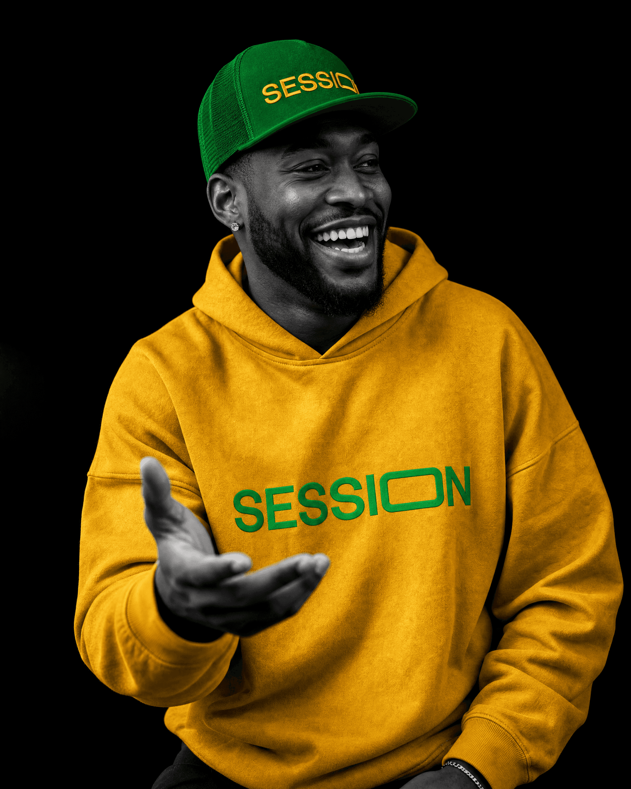 Man laughing and gesturing in a green Session Zone logo cap and yellow hoodie.
