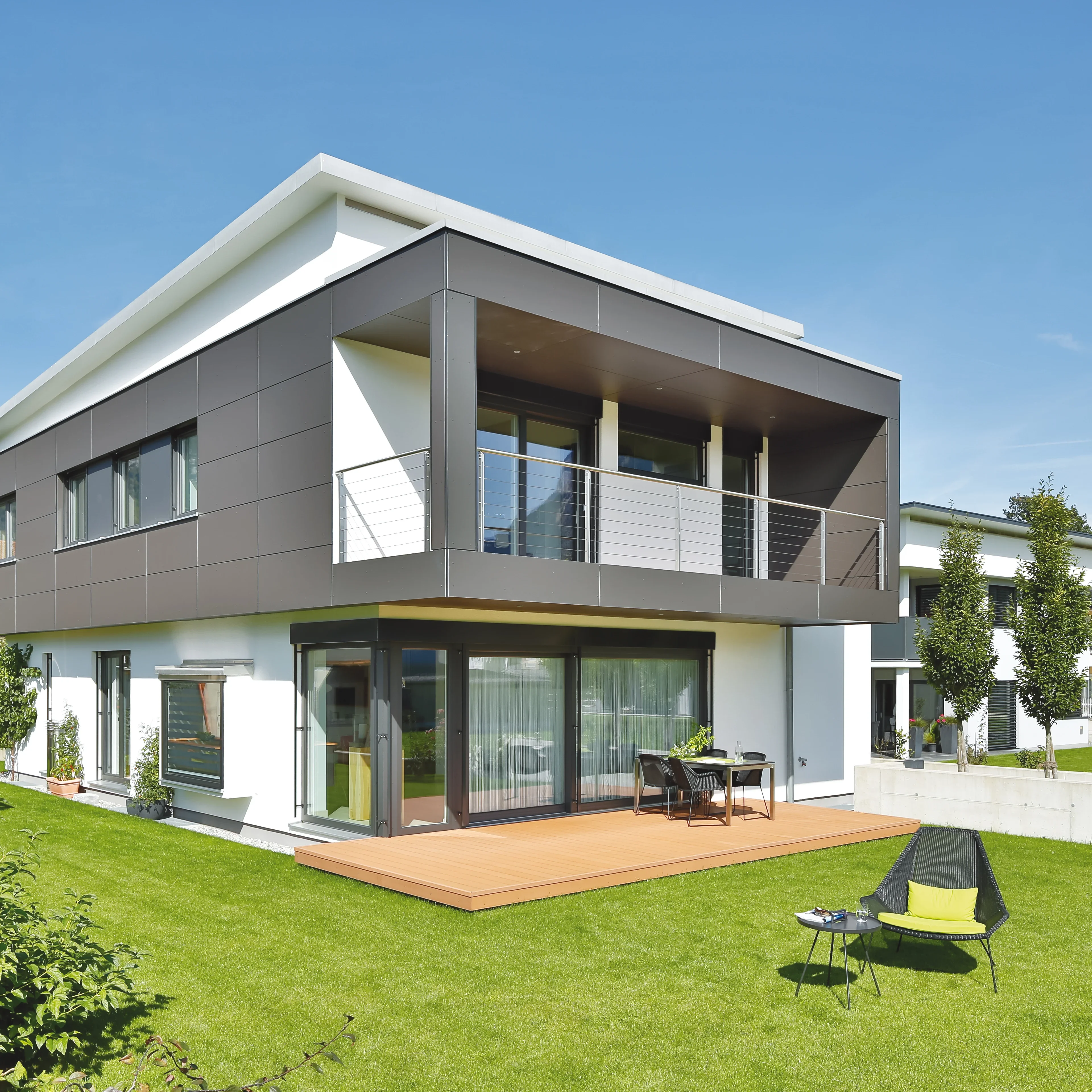 Modernhaus mit dunklen Fassadenplatten, großflächiger Verglasung, Terrasse und gepflegtem Rasen.