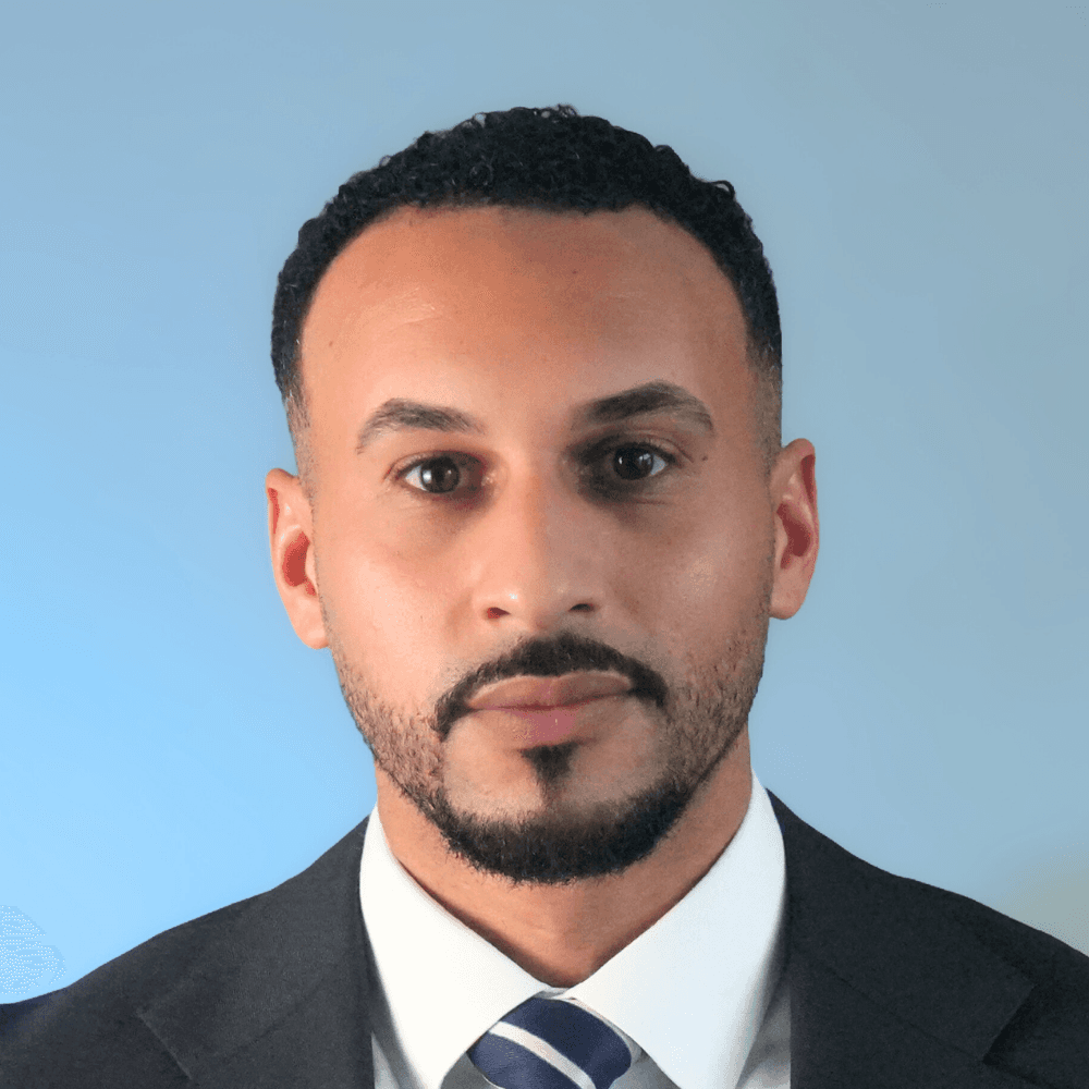A woman with short curly hair wearing a black t-shirt looks into the camera.