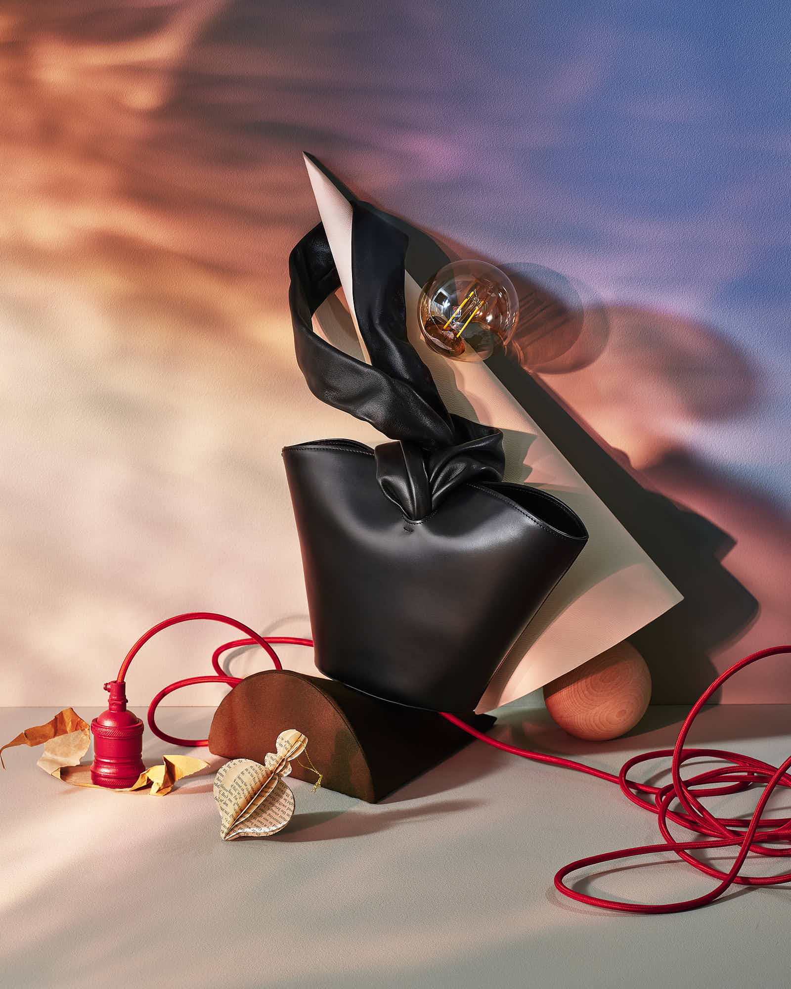 Stylish black leather handbag with artistic backdrop, red cord, and abstract decor elements.