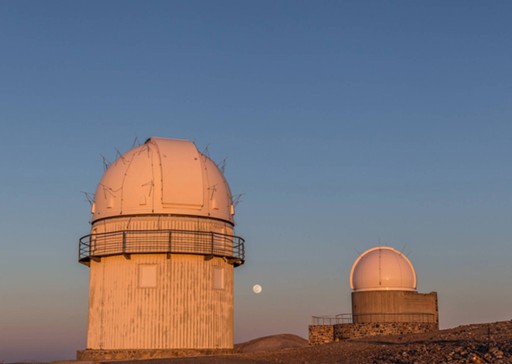 Δύο αστεροσκοπεία σε ορεινό τοπίο, με το φεγγάρι να ανατέλλει στον καθαρό νυχτερινό ουρανό.