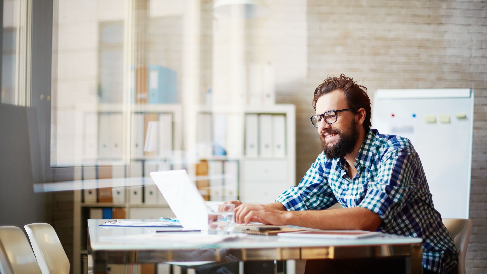A man smiles while working at his laptop in an ordinary office