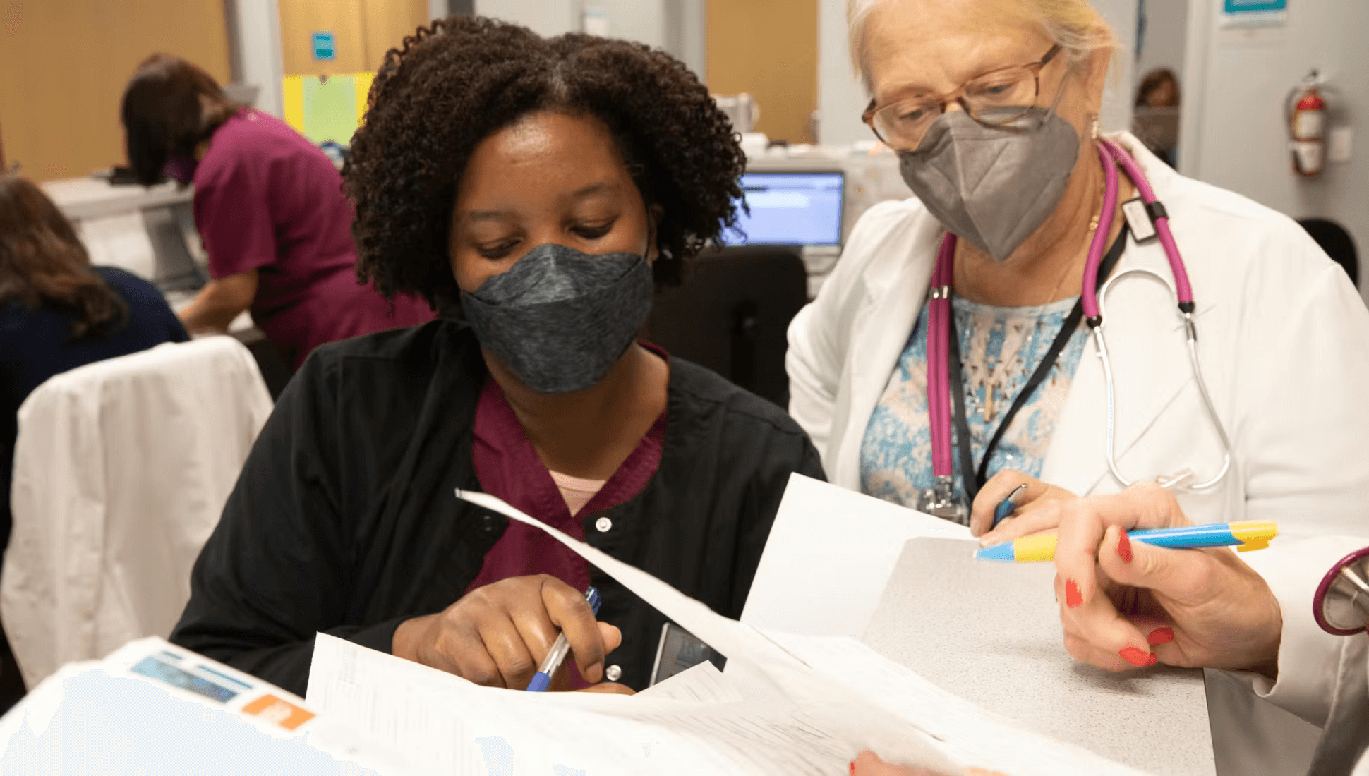 two nurses wearing a face mask while talking over some files