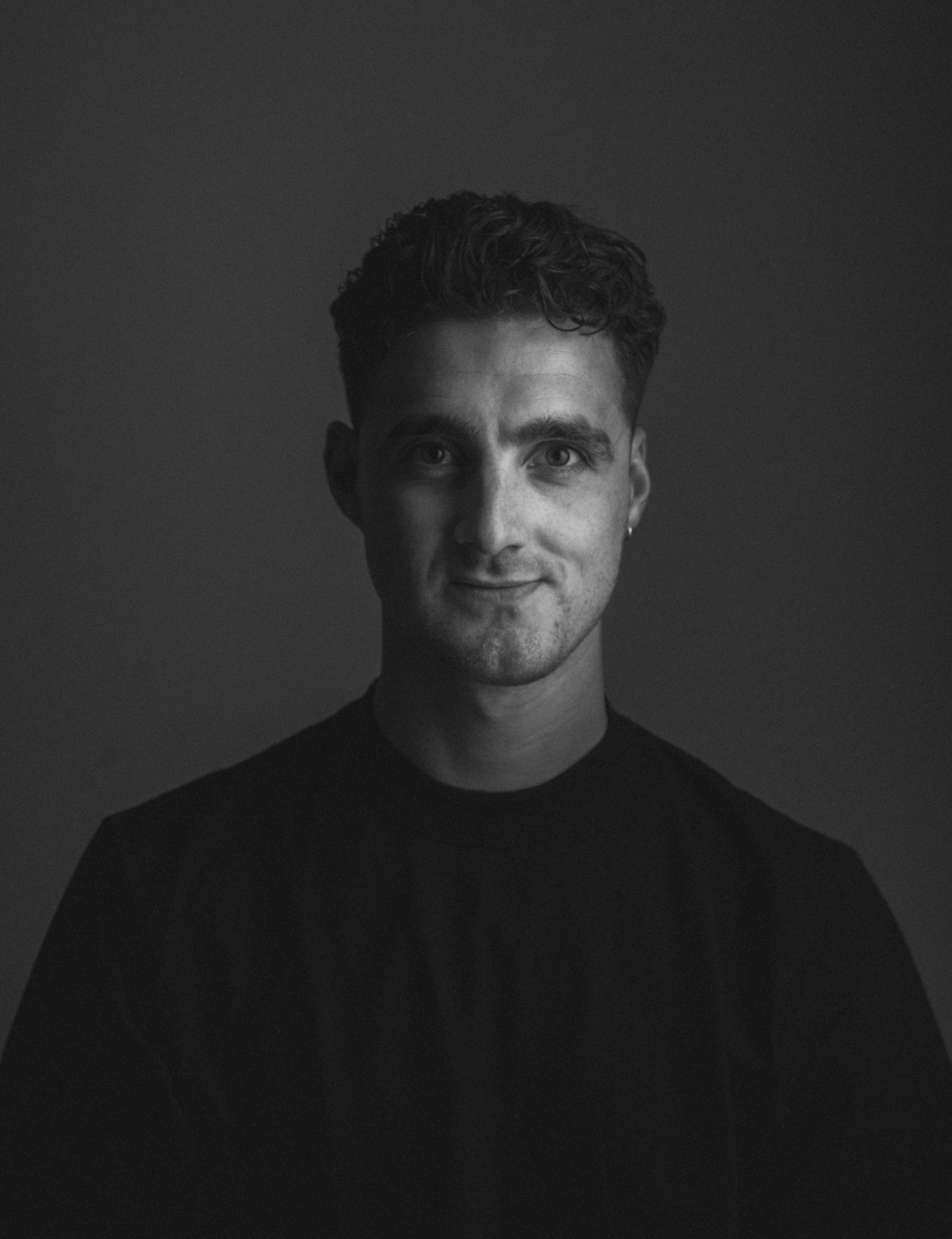 Black and white studio portrait of a man with short curly hair in a black T-shirt