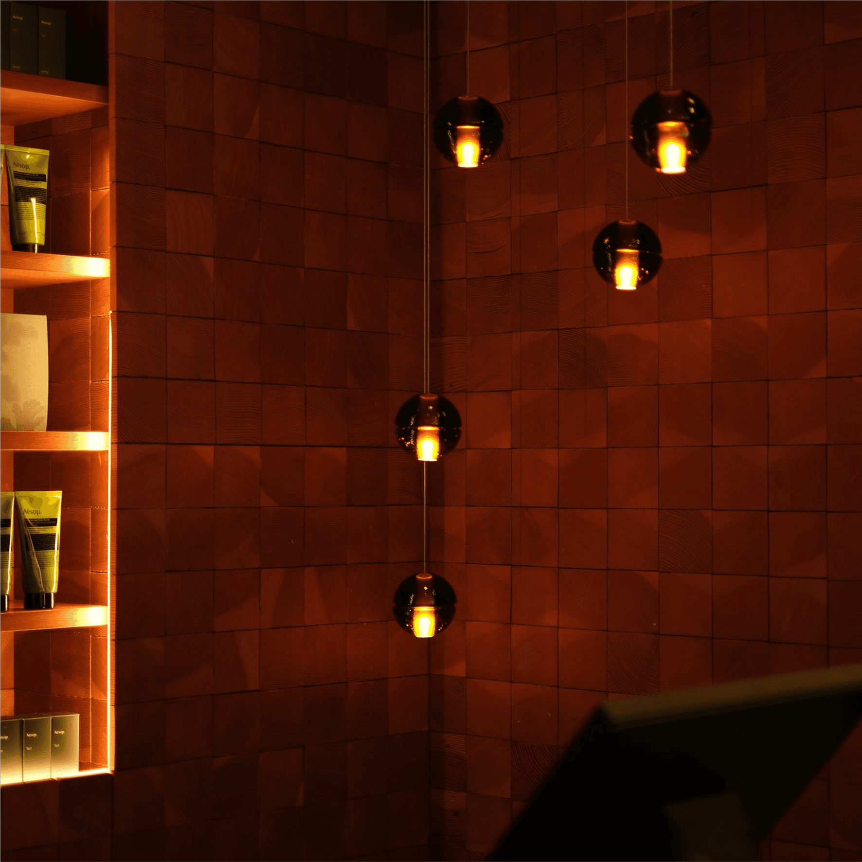 This warm, ambient-lit interior features a modern wall with illuminated shelving showcasing skincare products, alongside three hanging pendant lights casting a soft, golden glow, perfect for creating a soothing atmosphere.
