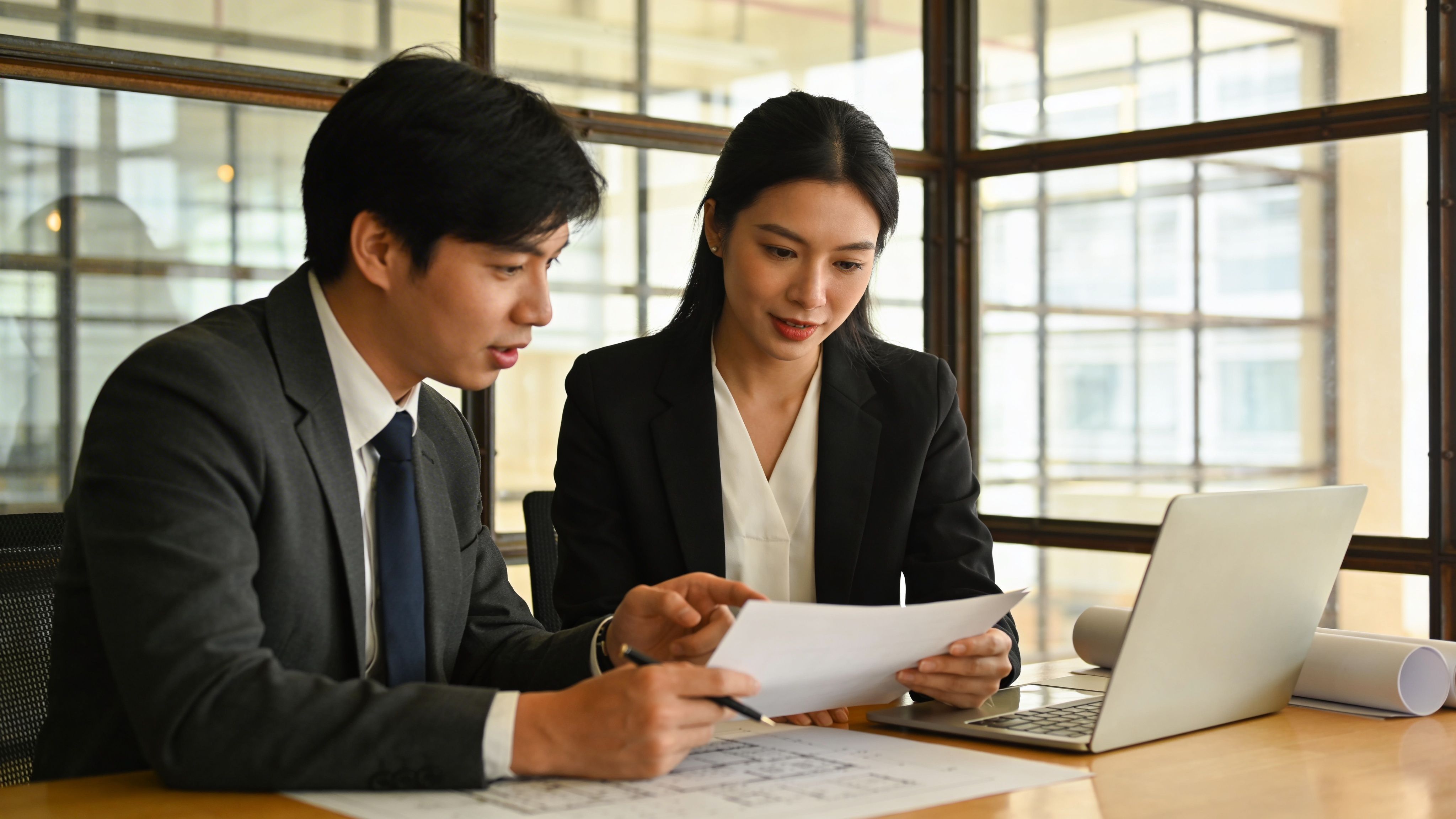 Business professionals reviewing documents together on a laptop in a bright office environment