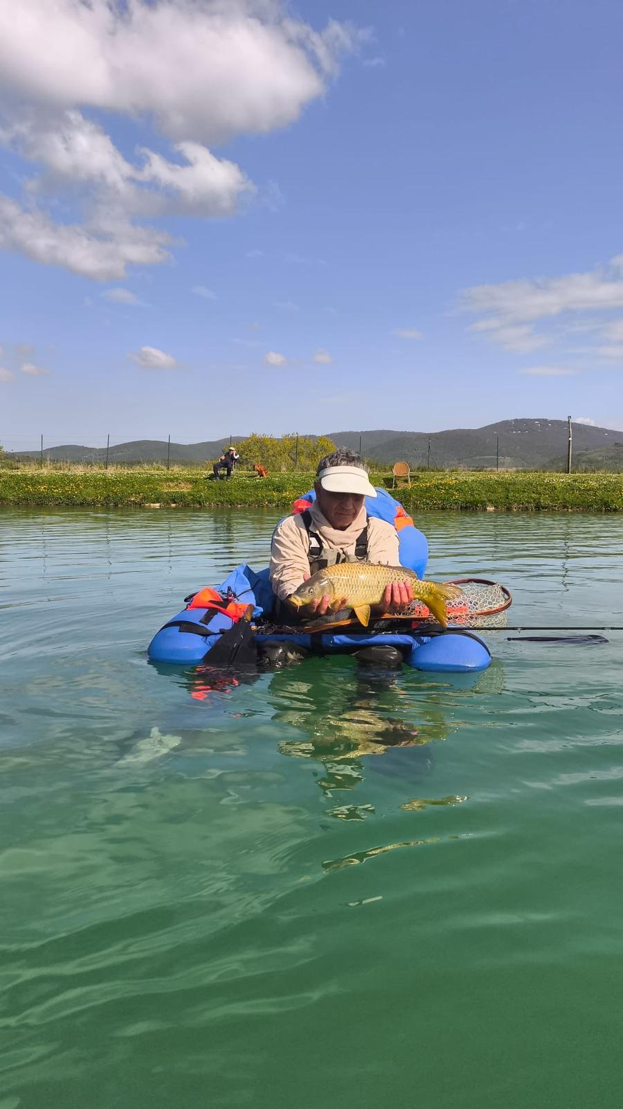 Angler in a belly boat holding a common carp on a reservoir