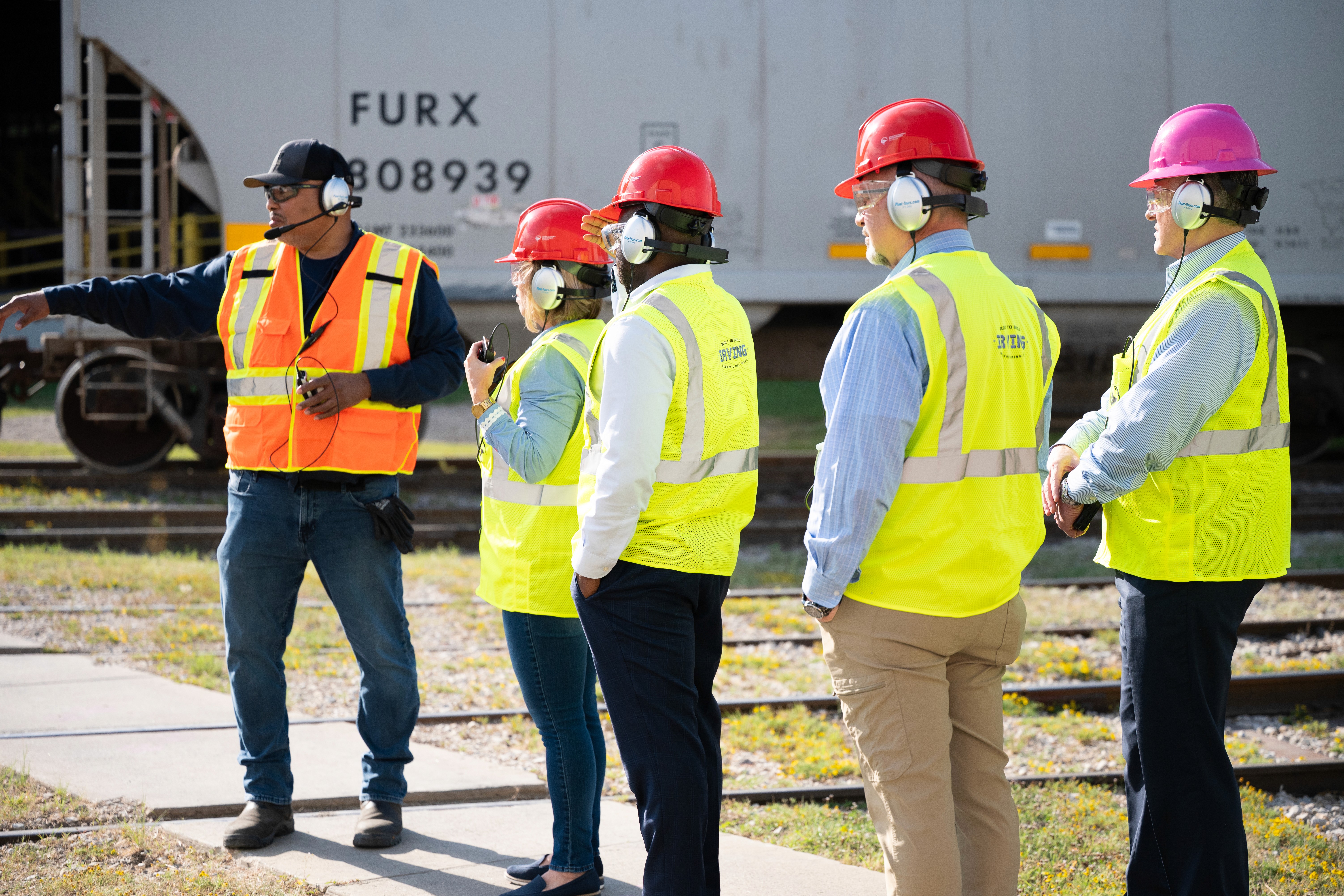 a group in construction vests and hard hats  experiencing a tour of a manufacturing facility. 