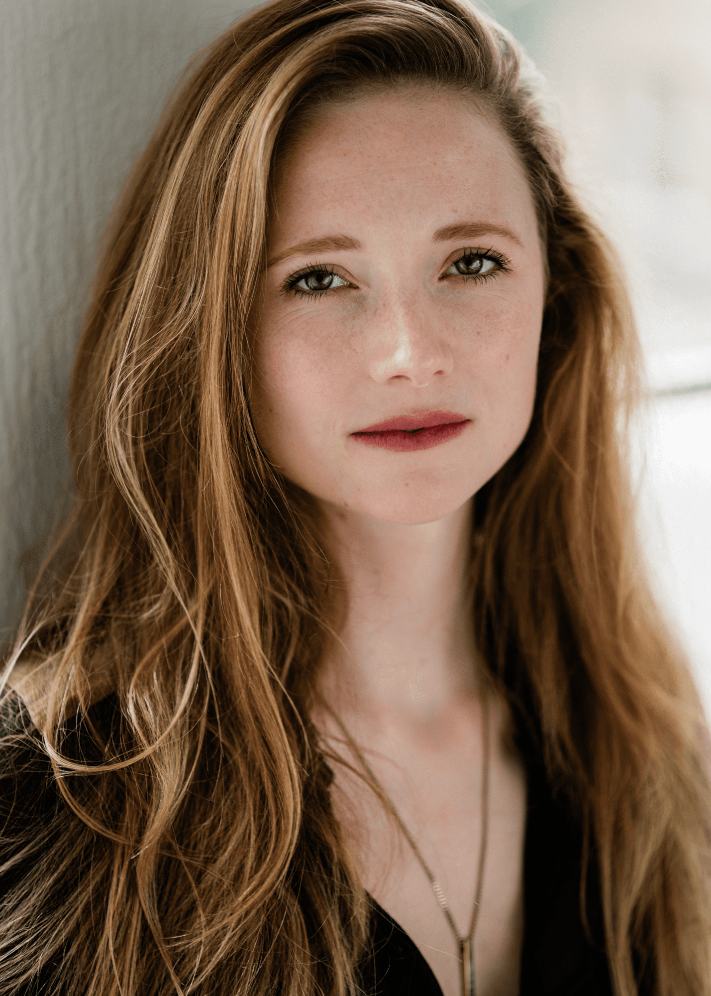 headshot casting photo of Joy Verberk, actor, long-haired woman in beige top, softly lit neutral background.