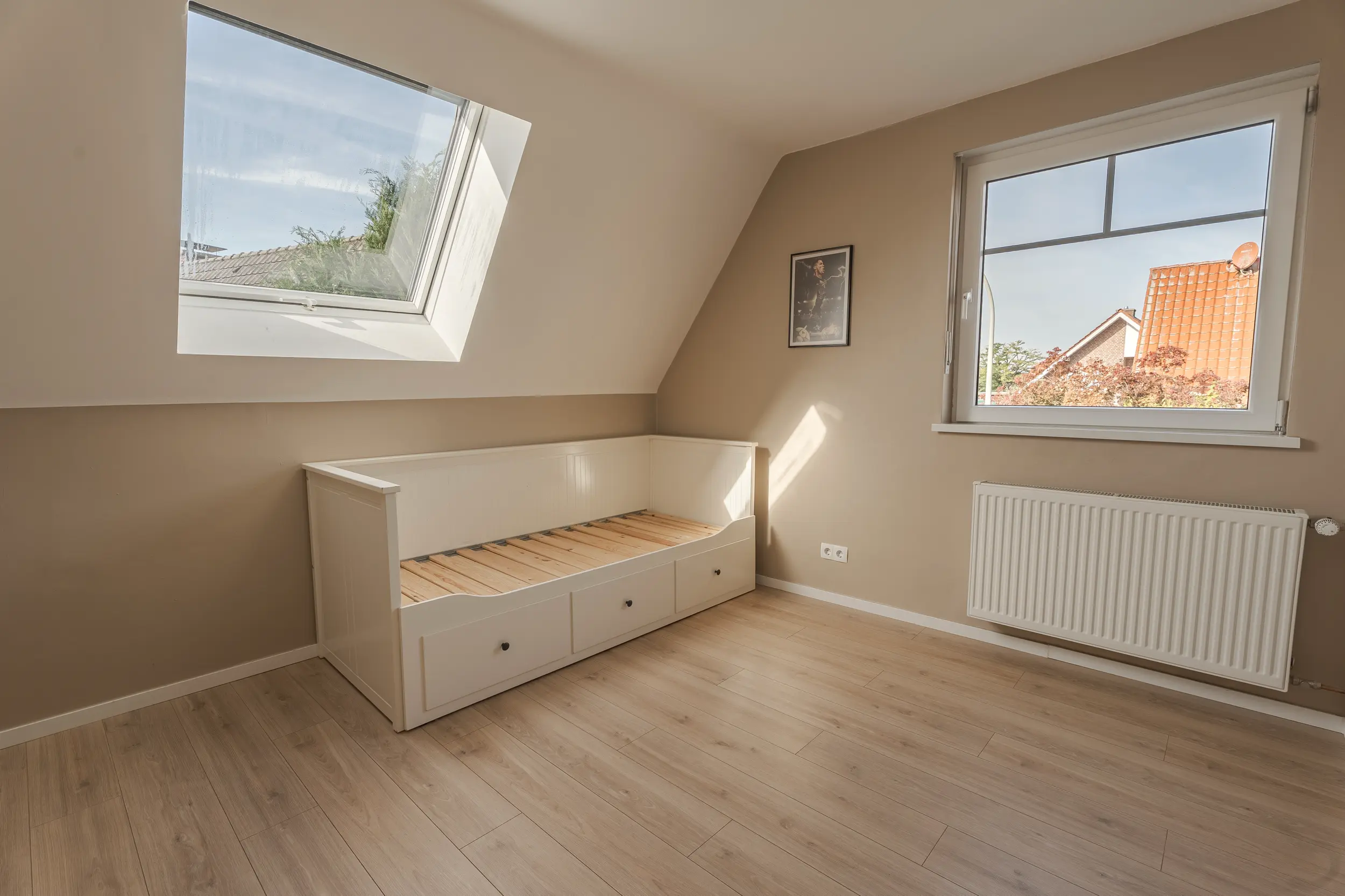 Zimmer im Einfamilienhaus in Südlohn-Oeding mit weißem Bettgestell, Dachfenster, Giebelfenster und hellem Boden.