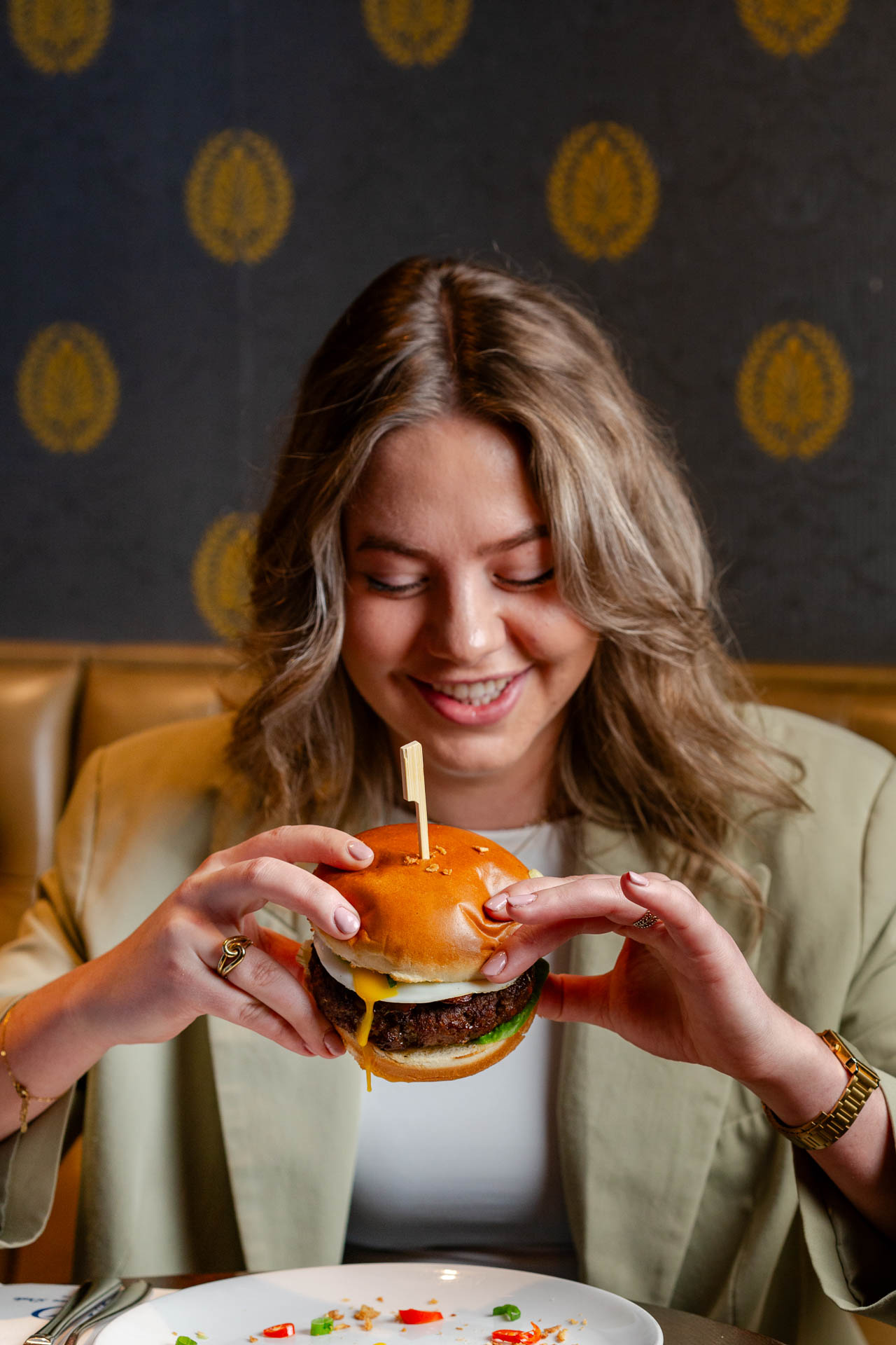 Een vrouw houdt een hamburger beet en kijkt er verlekkerd naar