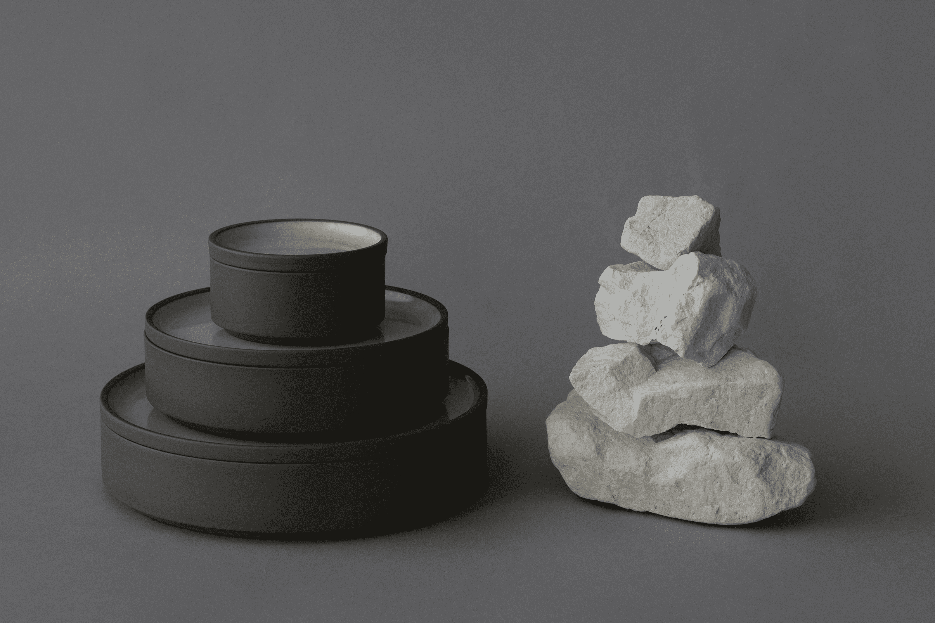 Stacked grey bowls and plates beside a stack of grey rocks