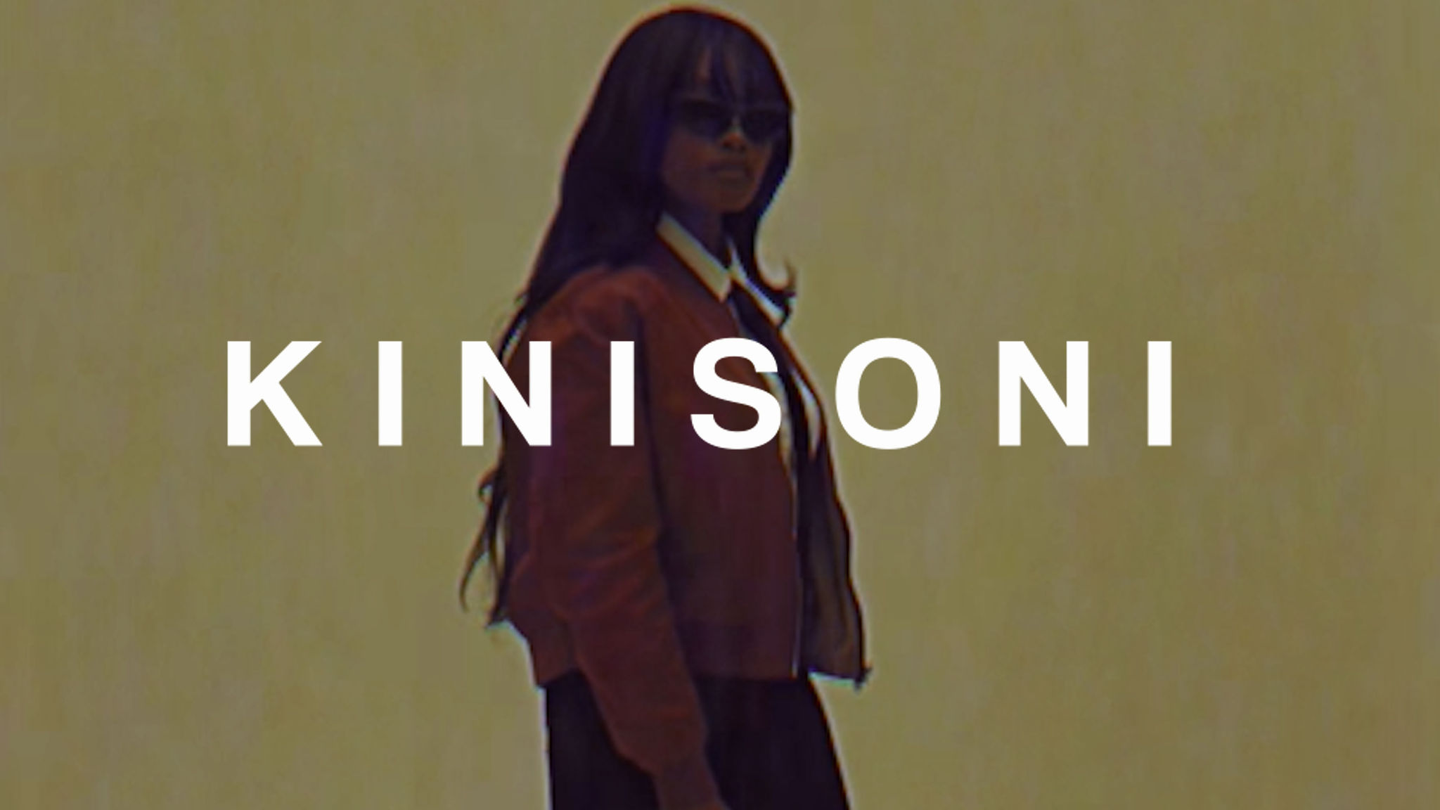 Man in letterman jacket and brown pants sits.