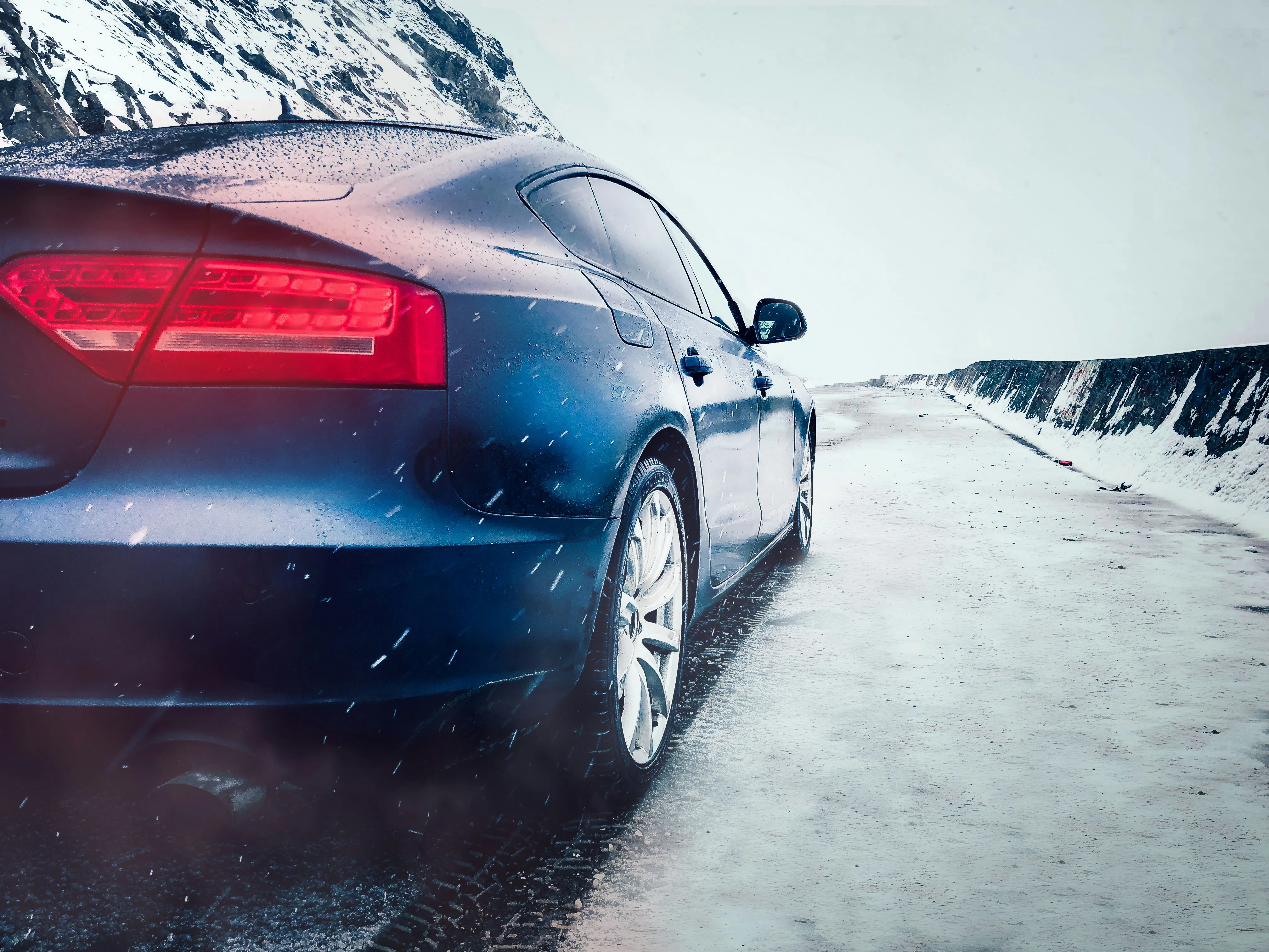 Rear view of a blue sedan driving on a snow-covered road