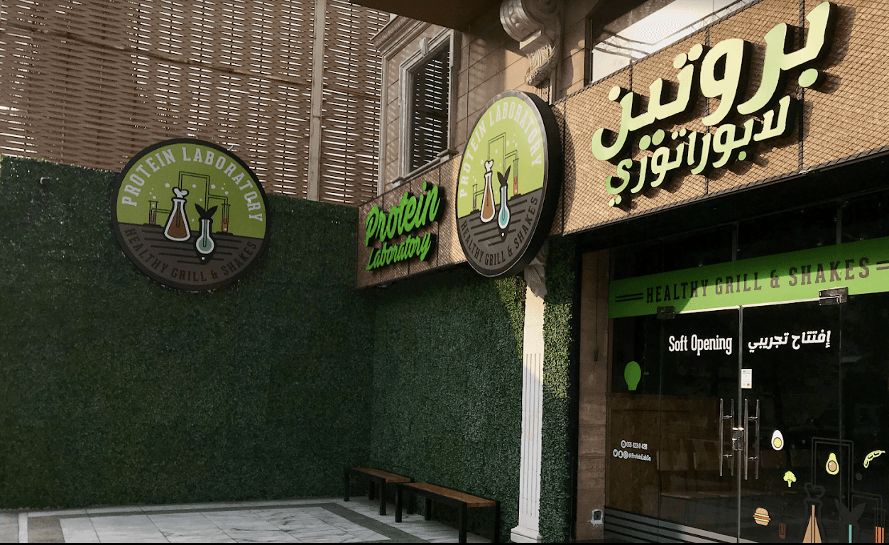 An overhead shot of a large oval plate featuring sliced, roasted duck, half glazed with a sauce, served over two thin pancakes and alongside steamed bok choy, surrounded by small bowls of condiments like scallions, sauce, salt, and carrot shreds.