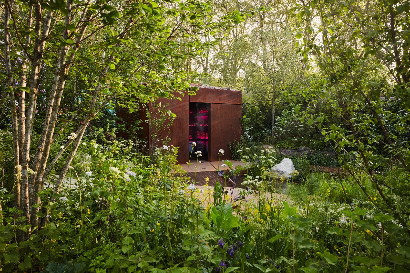 A tranquil garden pathway surrounded by lush greenery and blooming flowers, leading to a rustic wooden shed.