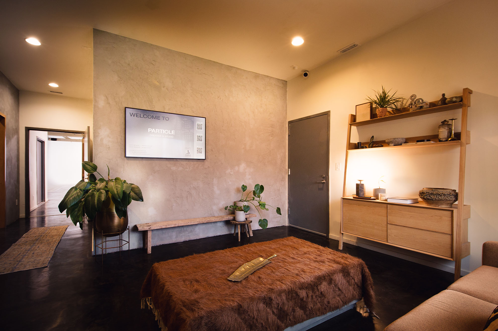 The studio floor is visable from the lobby of Particle Studios in Seattle, WA. There is a TV across from the couch that displays the name "Particle Studio" and hosts some other information about the space such as WIFI and the contact of the person working the studio.