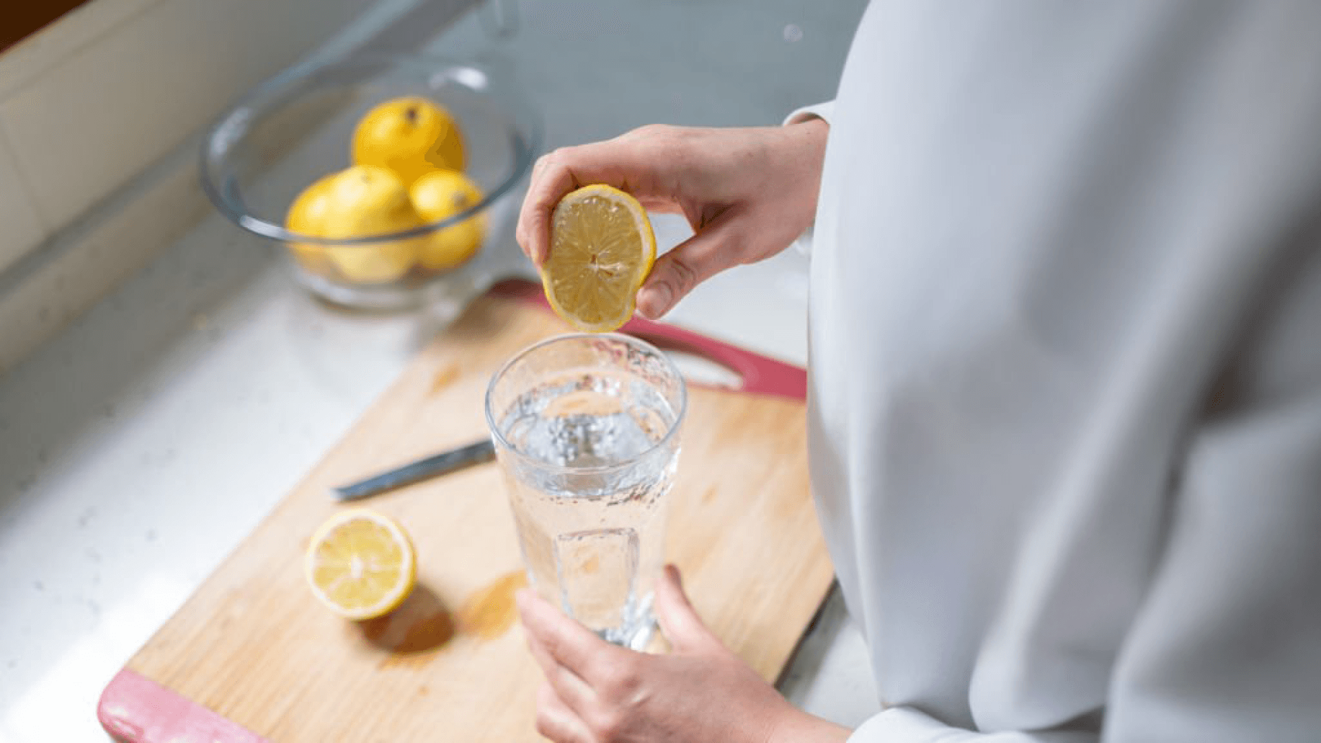 Squeezing lemon into a glass of water for a refreshing detox drink on a wooden cutting board.