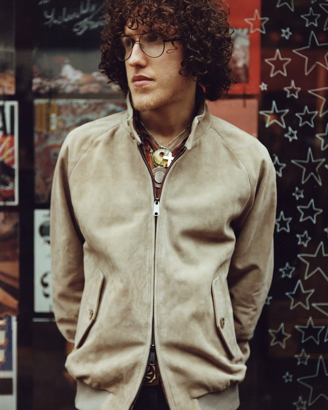 Le mannequin aux cheveux mongs porte un blouson en veau velours beige à double fermeture à glissière et des colliers esprit rock 