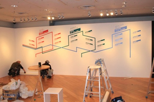poeple installing shelves and vinyl stickers on the wall for the ideopolis exhibition