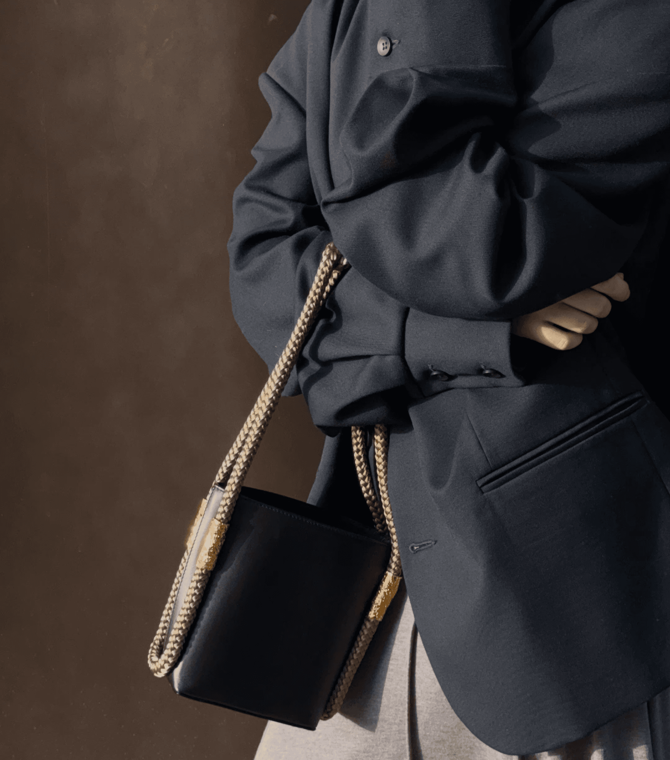 Brown sculptural leather handbag resting on tall ornamental grass during golden hour, evoking a natural, elegant mood.