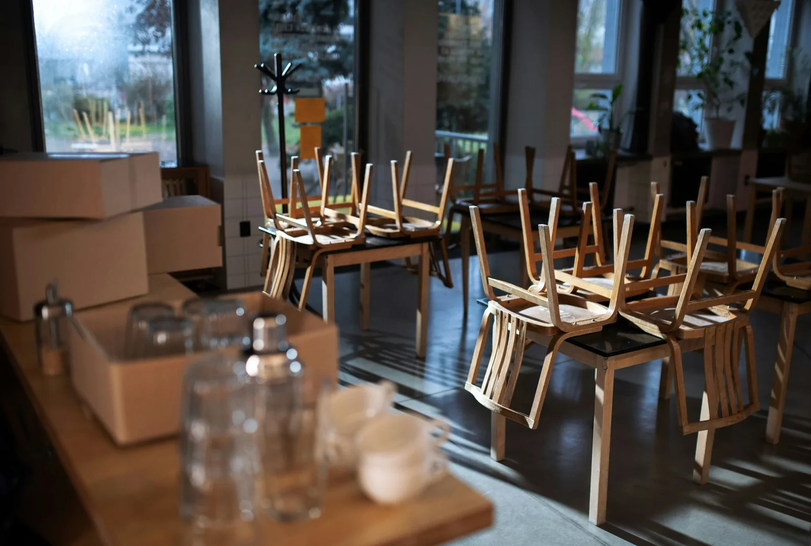 Empty restaurant dining room with wooden chairs and tables beside large windows, suggesting a slow business period.