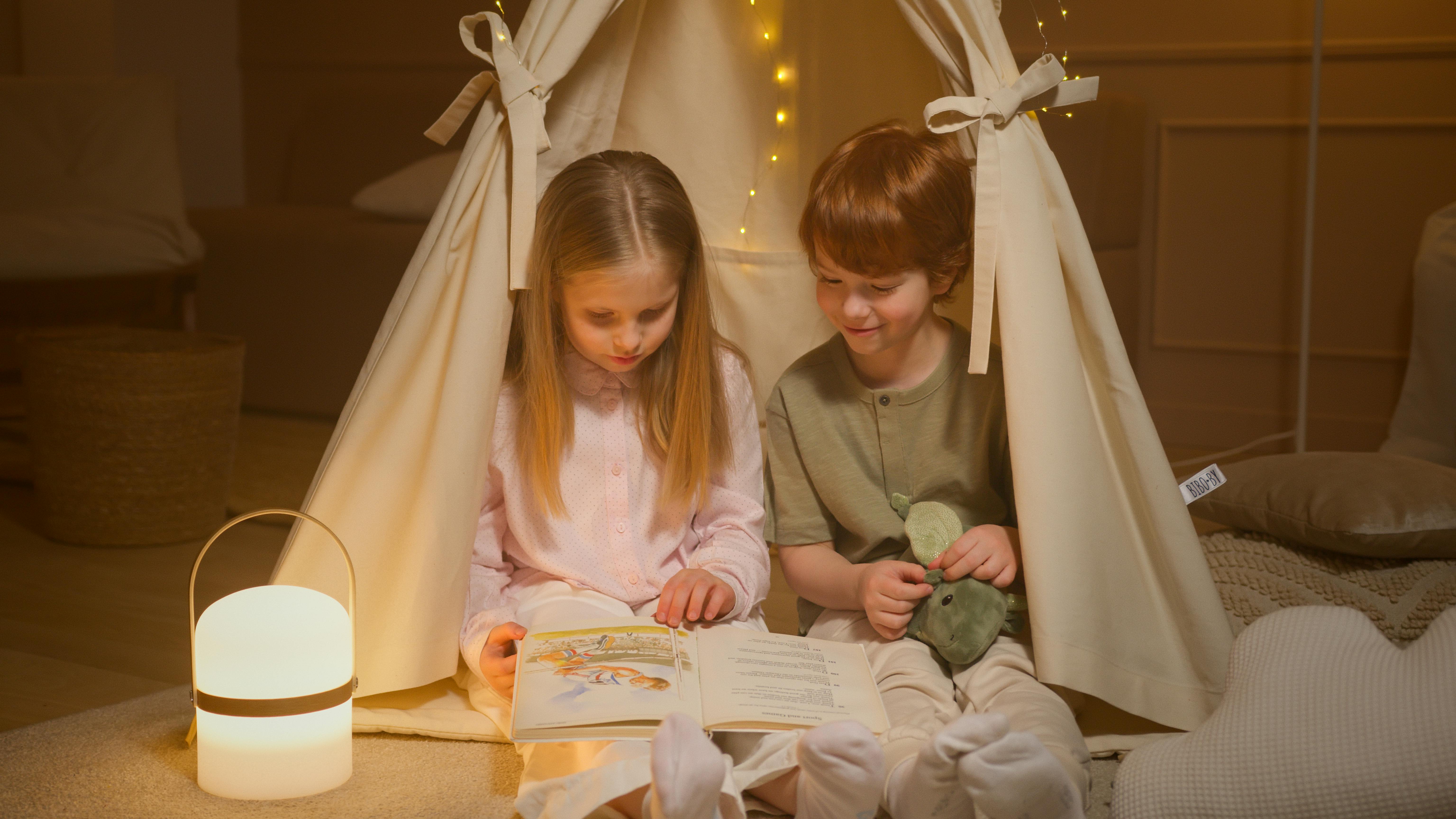 Children reading a book under a tent in the house