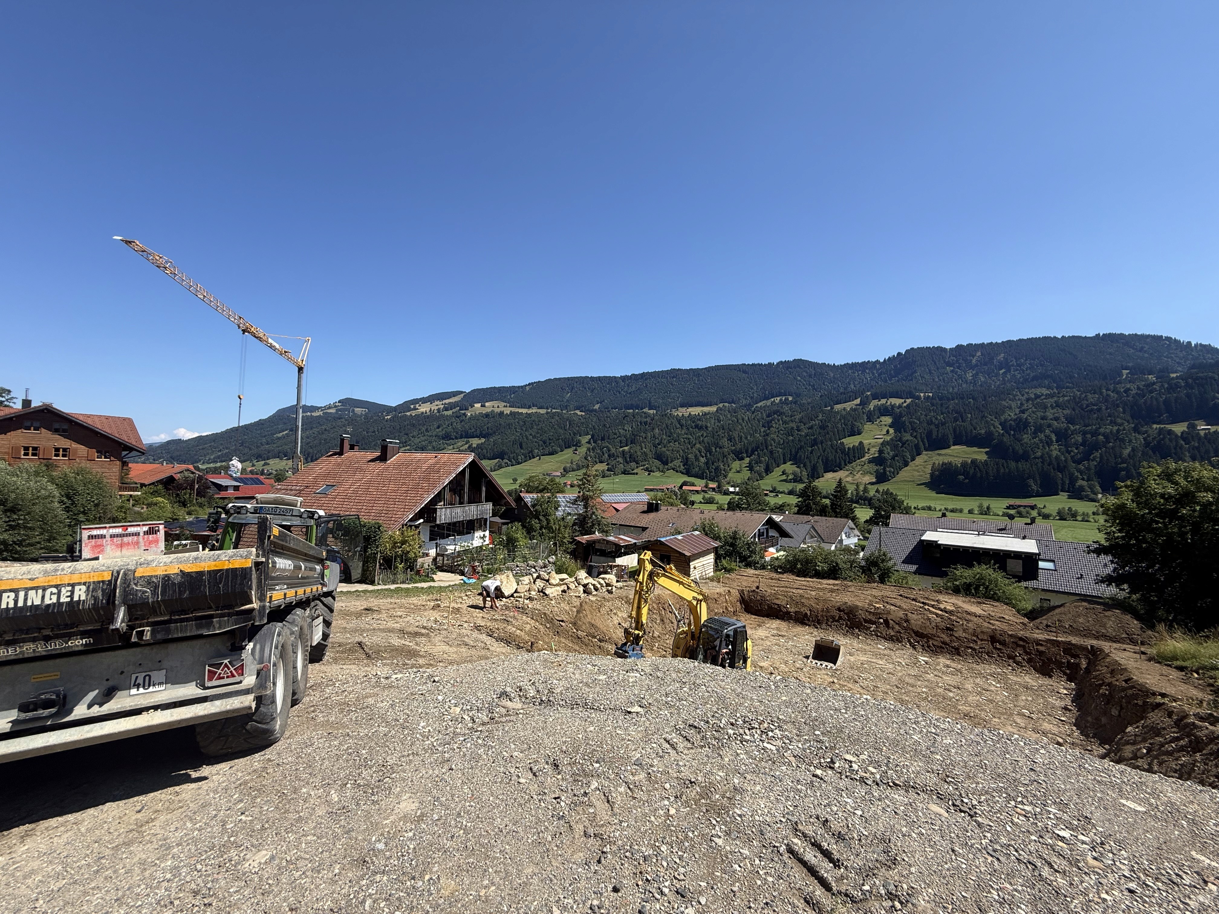 Baustelle des Wohnprojekts in Oberstaufen während der Aushubarbeiten mit Bagger, Kran und Baustellenfahrzeug