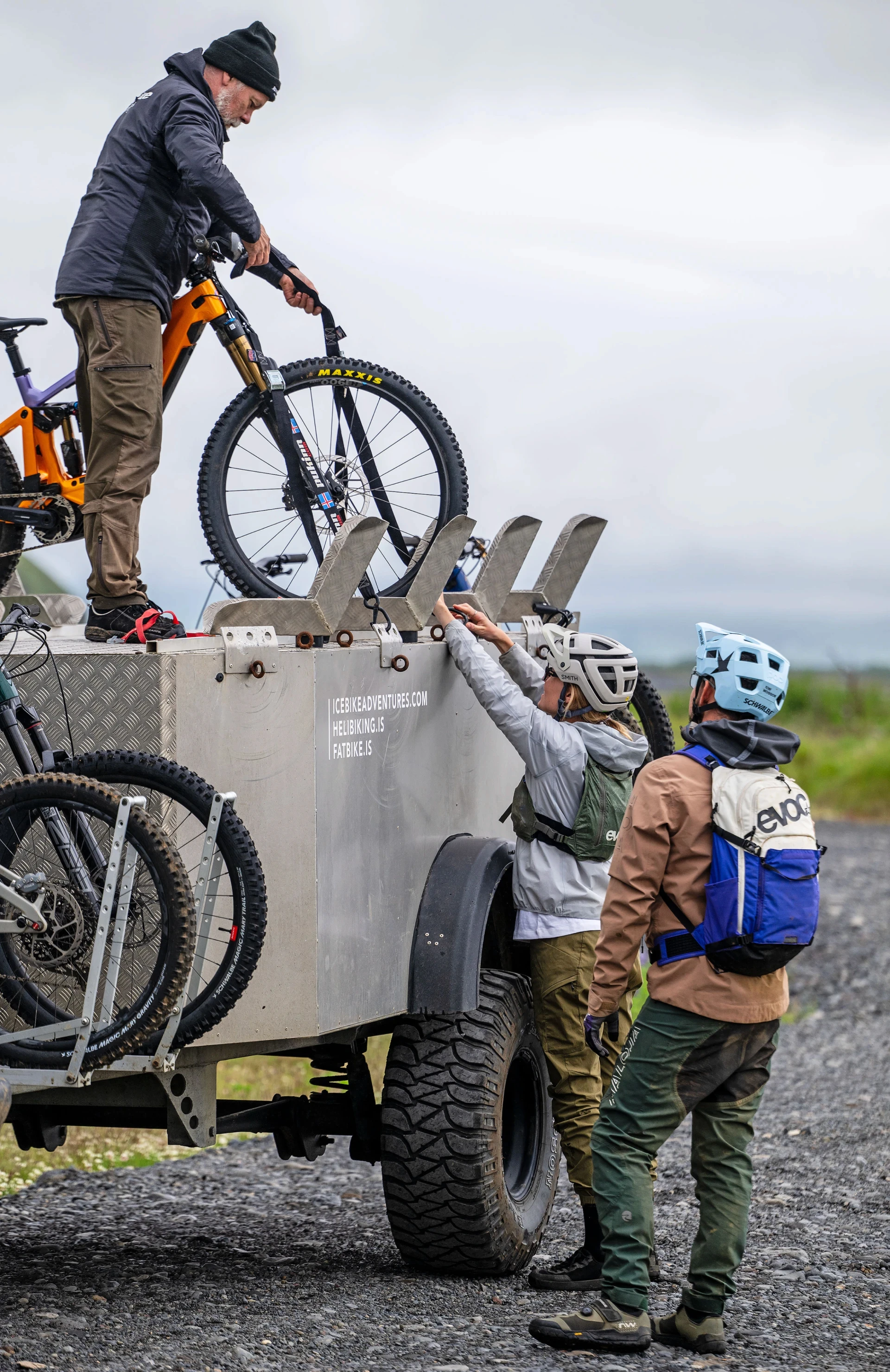 Man handing bike down to another from a big bike trailer