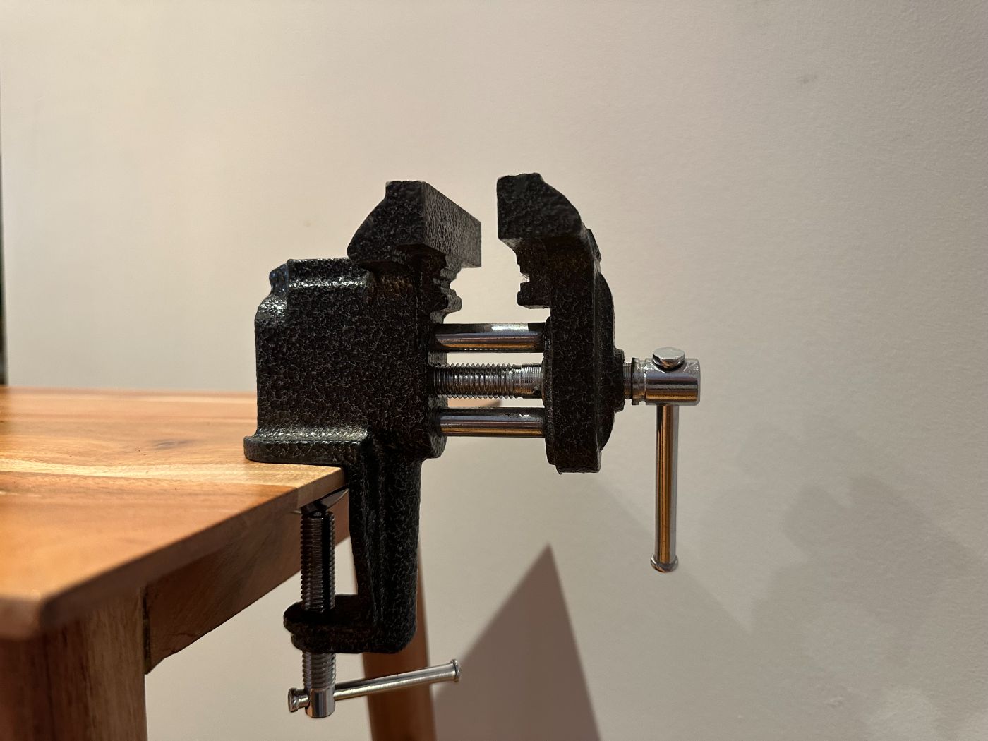 Petit étau de table en métal noir fixé sur un plan de travail en bois, vu de côté