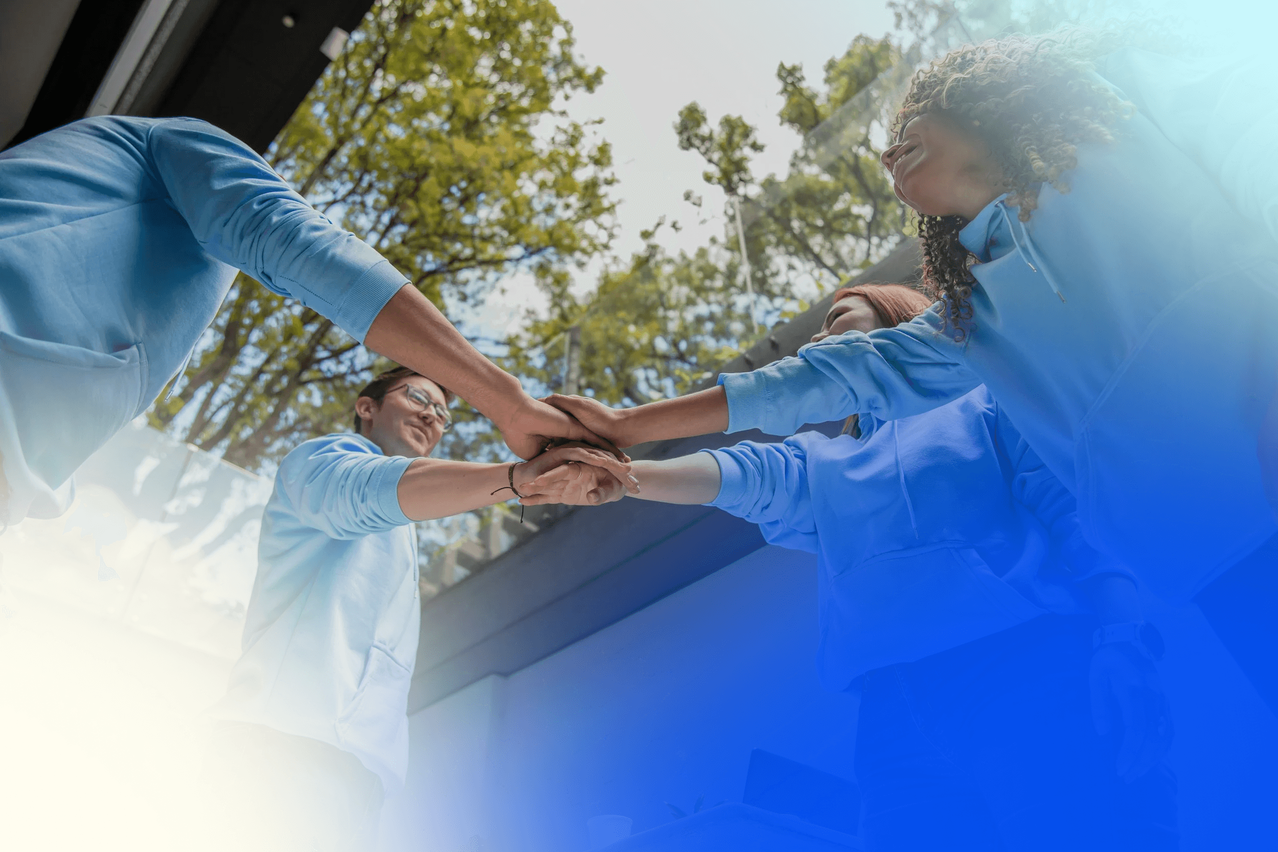 our people in light blue hoodies putting their hands together outside, symbolizing teamwork and unity.
