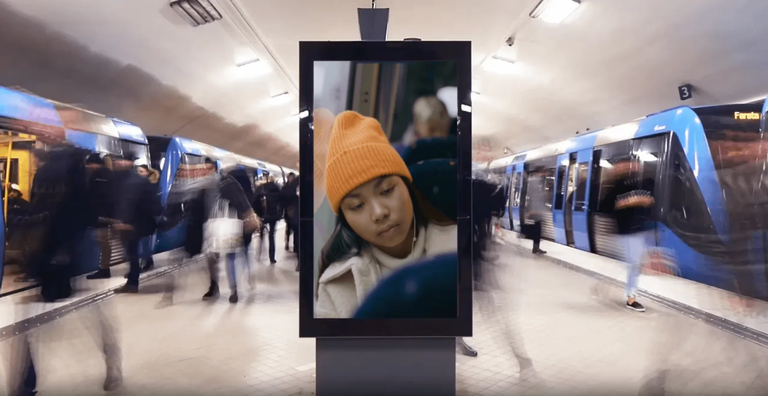 Digital reklamskylt på en tunnelbaneperrong med resenärer i rörelse