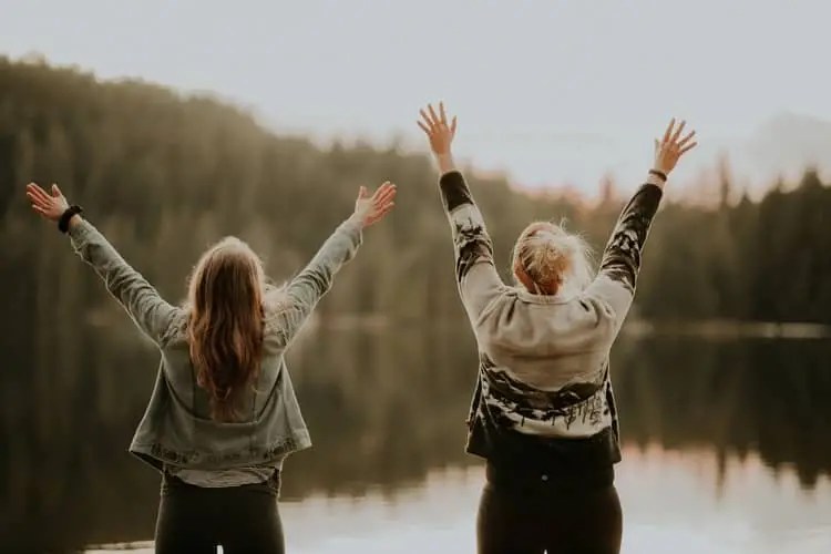 two women with arms outstretched towards the sky standing with their backs facing the camera
